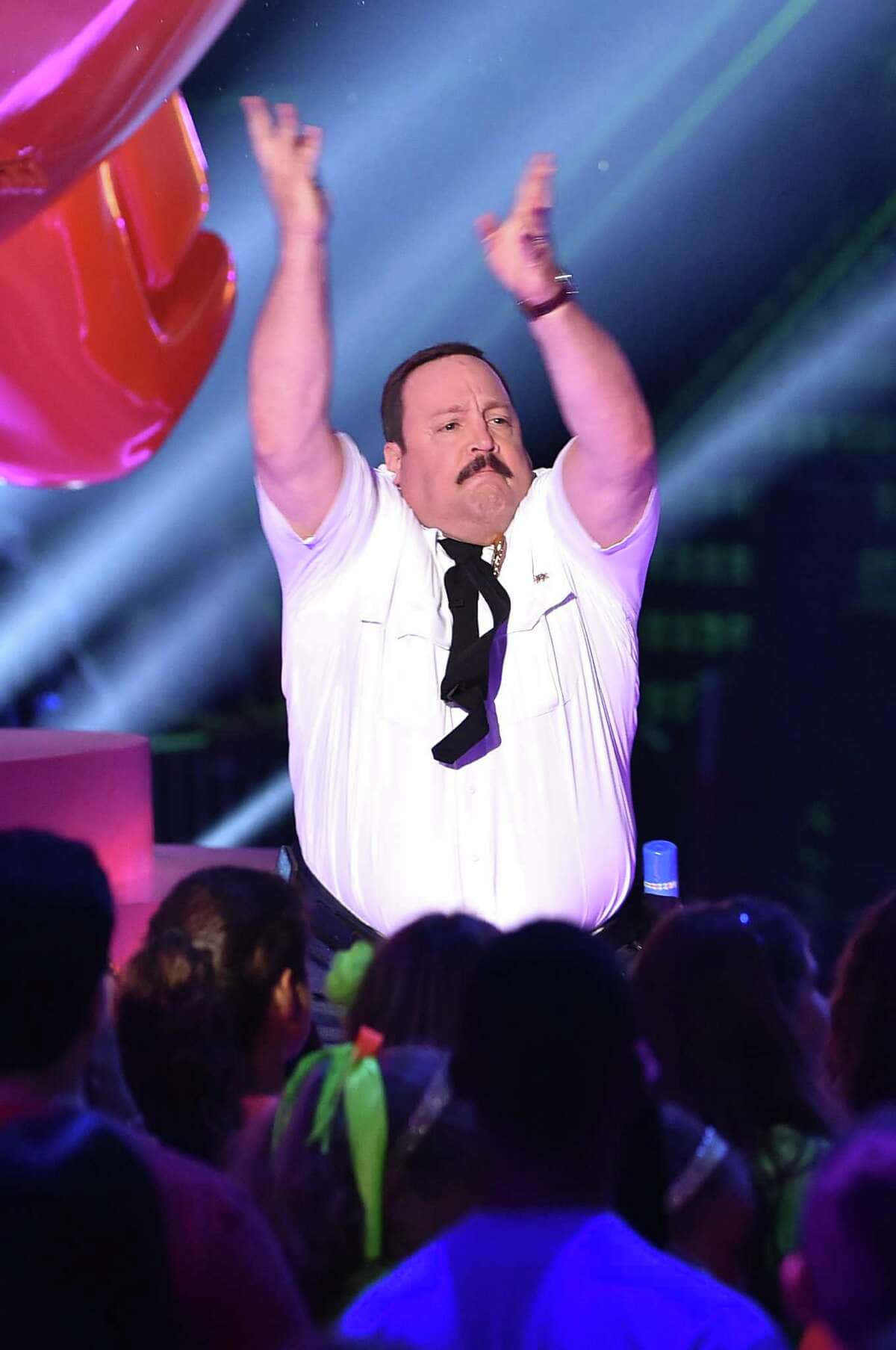 Kevin James 桌布 壁紙 — 一個留鬍鬚嘅男人，著住白恤衫同黑色領呔，喺一個燈光燦爛、有彩色射燈嘅舞台上舉起雙臂，台下有群眾。