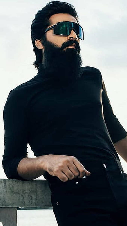 Indian 桌布 壁紙 — 一個留鬍鬚的男人，戴著黑色太陽眼鏡和 turtleneck，在陰天時隨意靠在混凝土欄杆上。