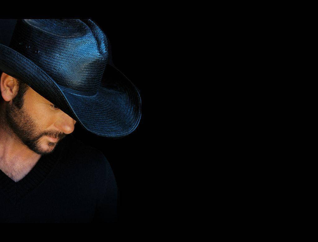 Tim Mcgraw 桌布 壁紙 — 一個留鬍鬚的男人戴著藍色牛仔帽，背景是純黑色，他的臉部分隱藏在陰影中。