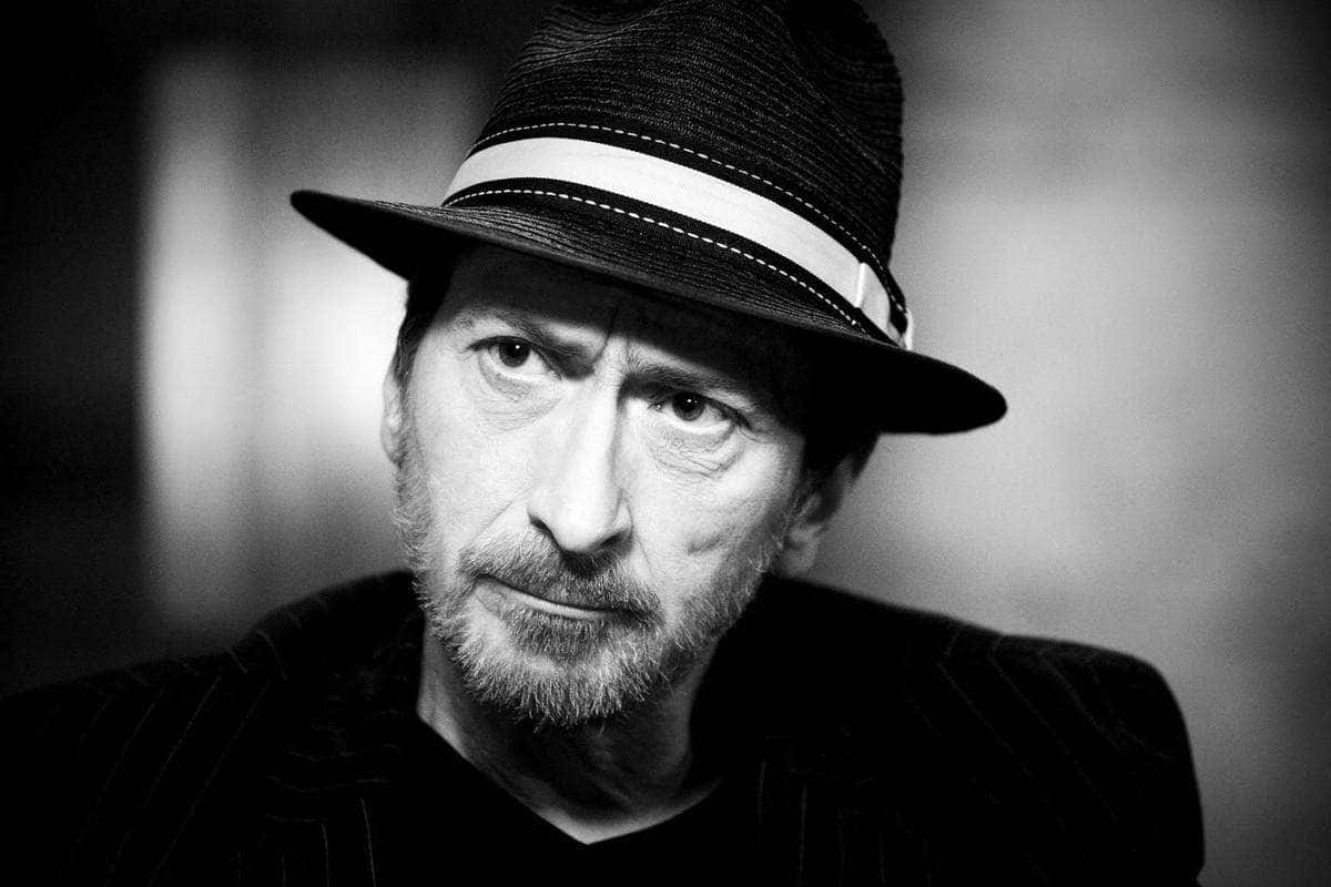 Frank Miller 桌布 壁紙 — 一個留鬍鬚的男人戴著軟呢帽和細條紋外套，強烈地凝視鏡頭的黑白肖像。