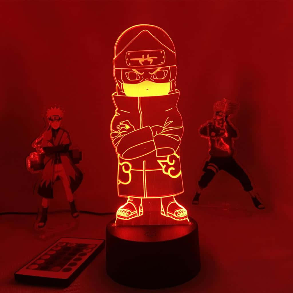 Akatsuki Kakuzu 桌布 壁紙 — 一個發光的3D動漫燈，形狀像蒙面忍者，在紅光中照亮，附近有兩個公仔和一個遙控器。