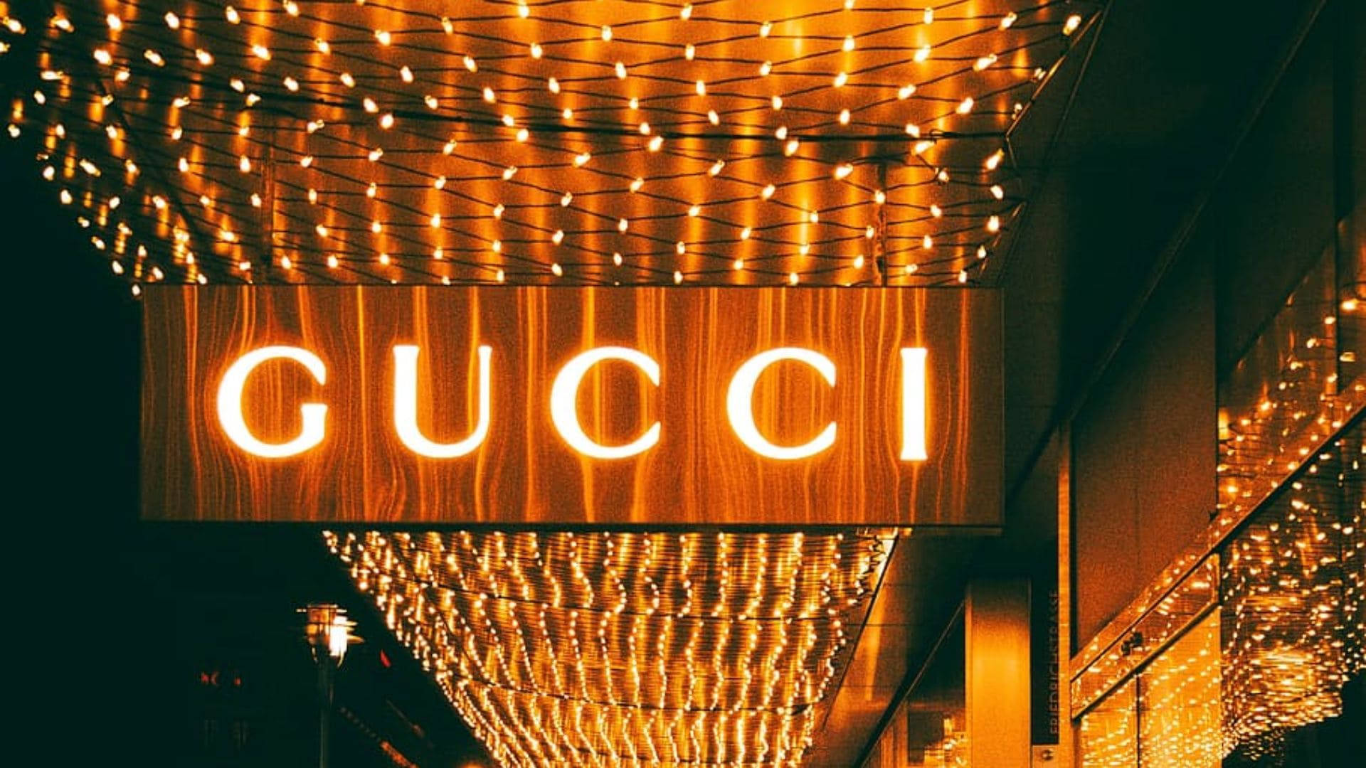 Gucci 桌布 壁紙 — 一個發光的Gucci標誌，被溫暖的串燈照亮，背景是黑暗的城市夜空。