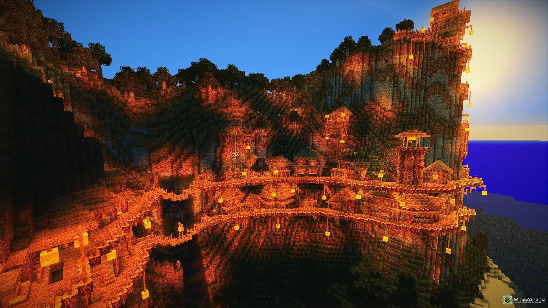 城堡 桌布 壁紙 — 一個發光的Minecraft村莊在日落時依附在懸崖邊，溫暖的燈籠照亮了深藍色天空下的石頭建築。