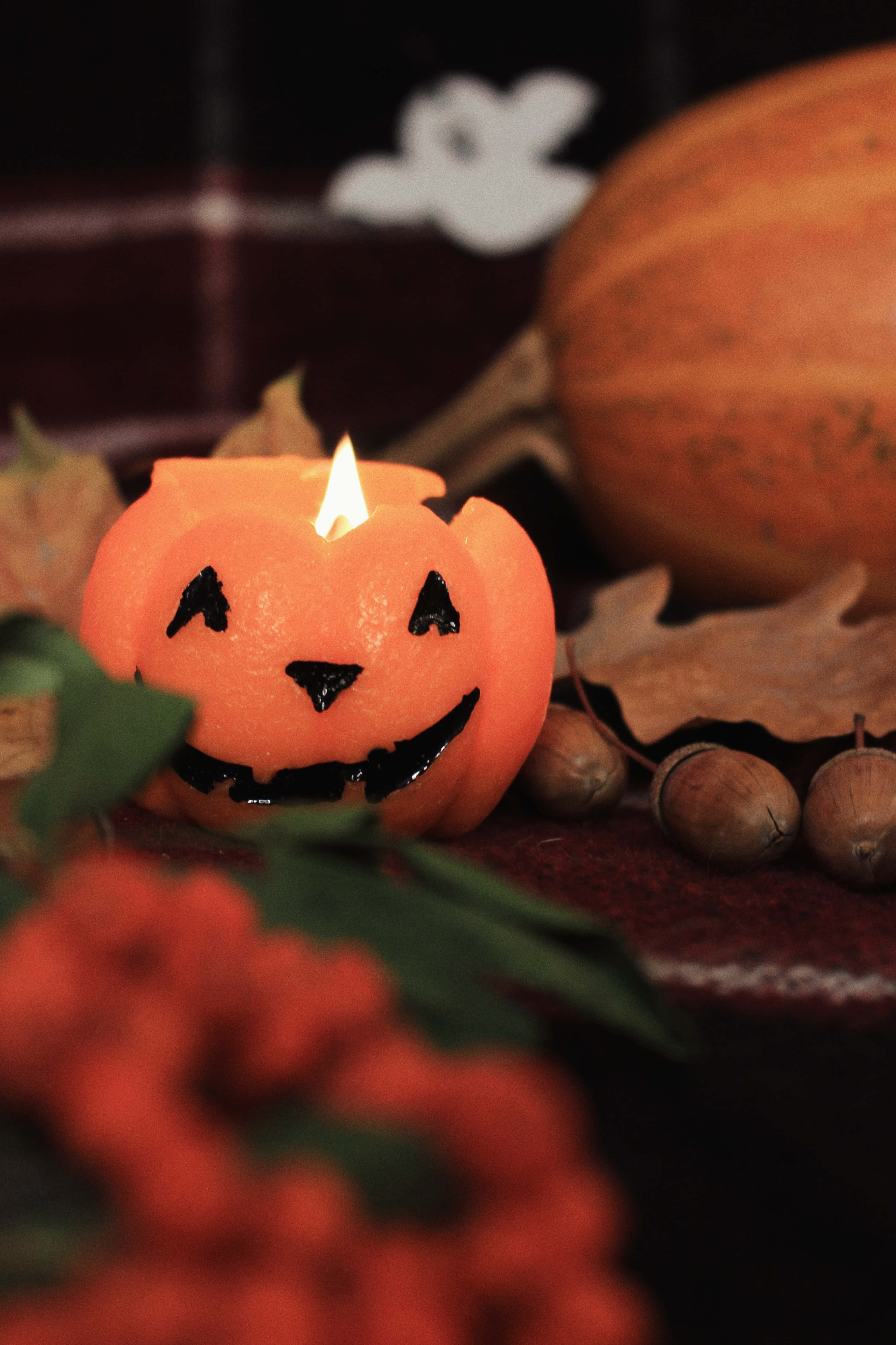 Halloween Phone 桌布 壁紙 — 一個發光的傑克南瓜燈蠟燭放在秋天的樹葉、堅果和南瓜之間，營造出舒適的萬聖節場景。