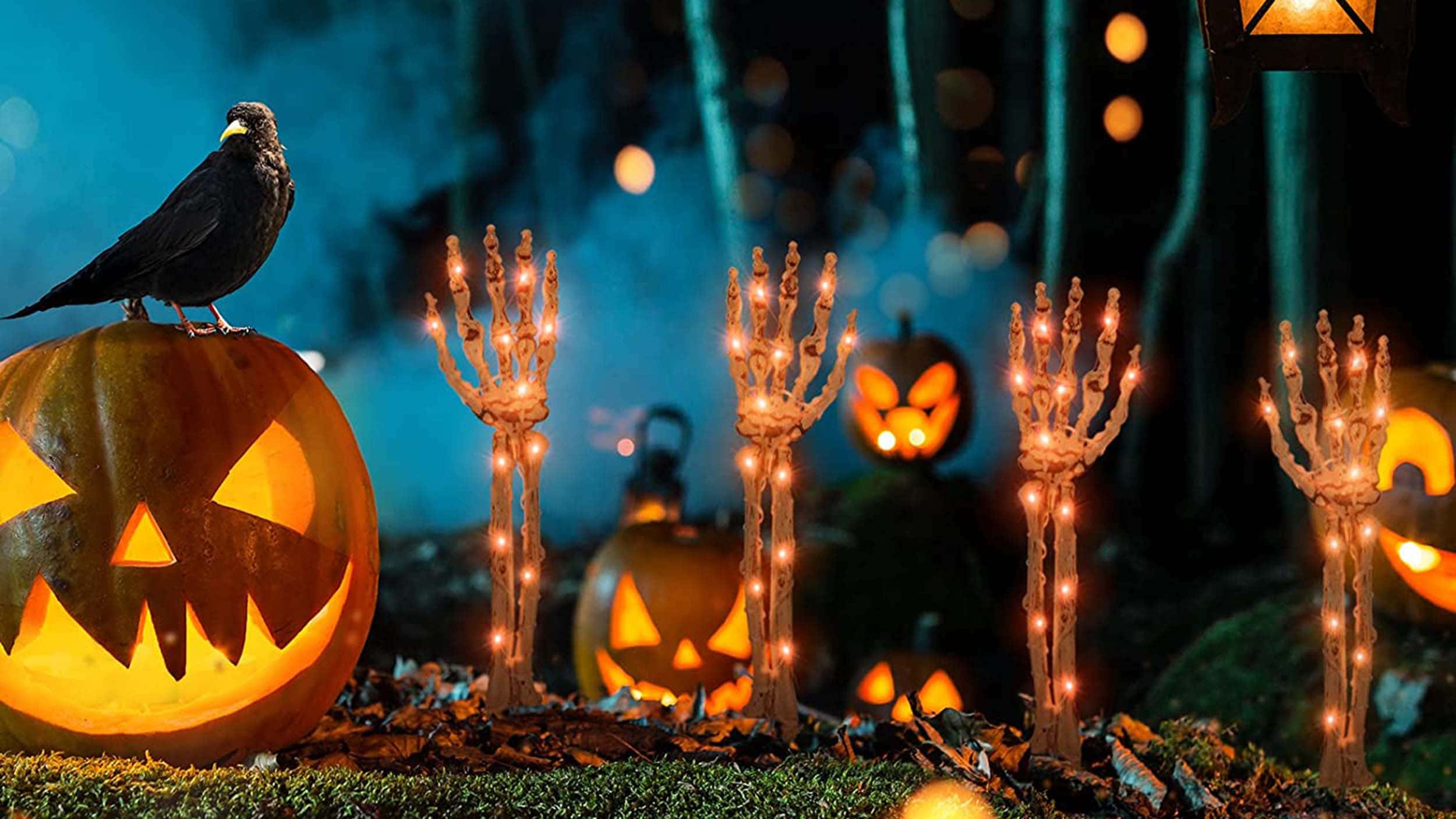 Halloween Props 桌布 壁紙 — 一個發光的南瓜，頂上棲息著一隻烏鴉，周圍環繞著骷髏手蠟燭，在夜晚的迷霧森林中。
