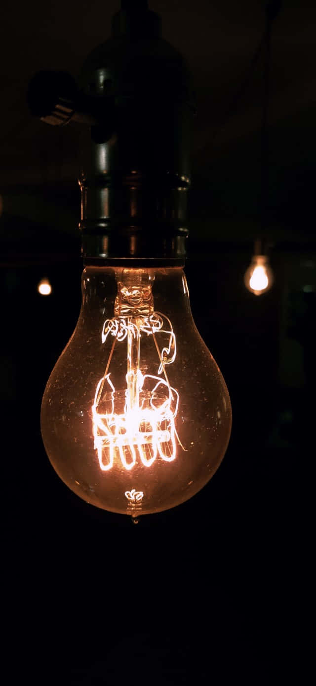 Electricity 桌布 壁紙 — 一個發光的復古燈絲燈泡懸掛在黑暗中，溫暖的光線投射出柔和的陰影，並突出內部複雜的線圈。