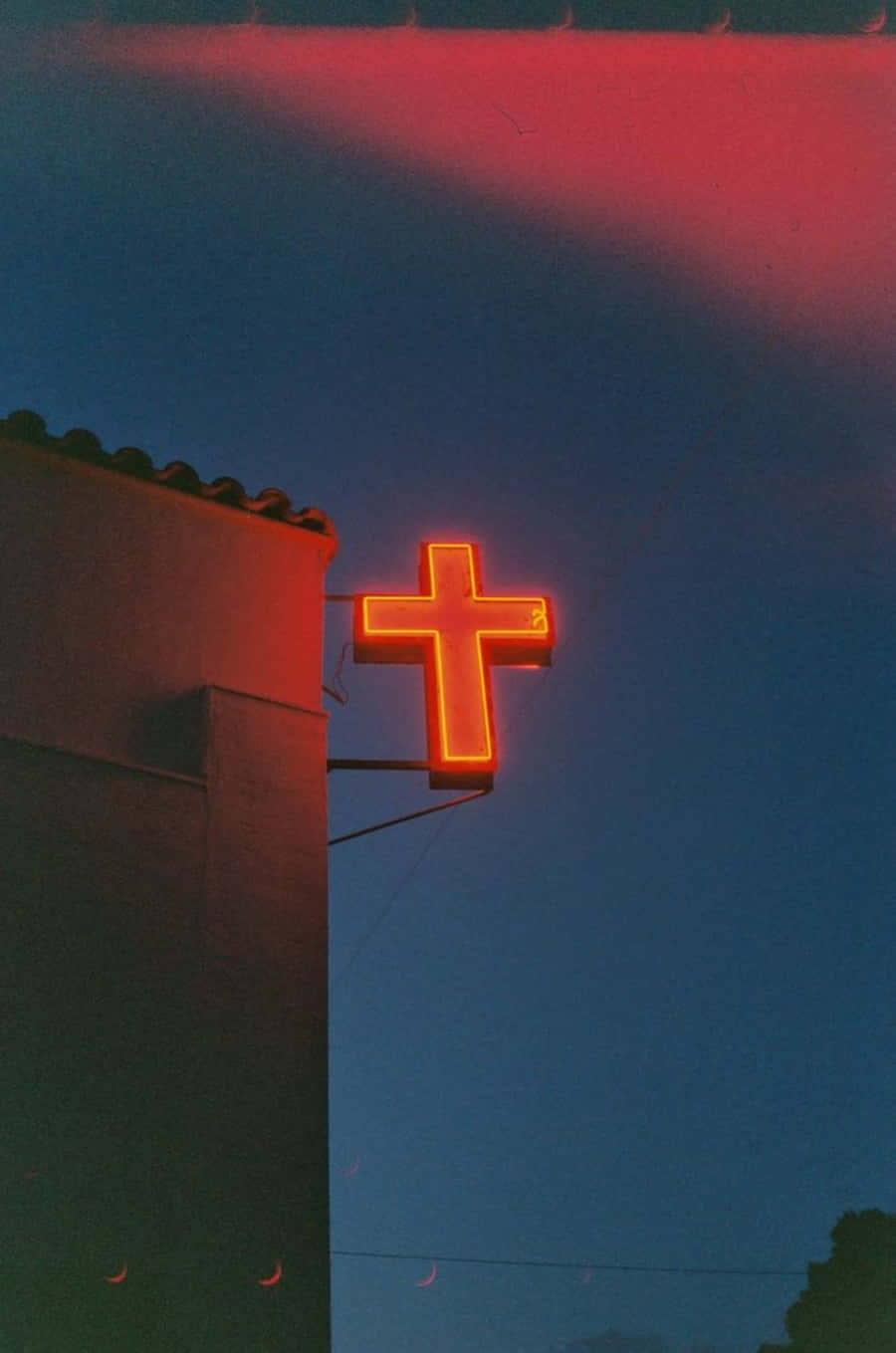 Cool Cross 桌布 壁紙 — 一個發光的橙色霓虹十字架標誌安裝在建築物上，背景是帶有粉紅色和藍色色調的黃昏天空。