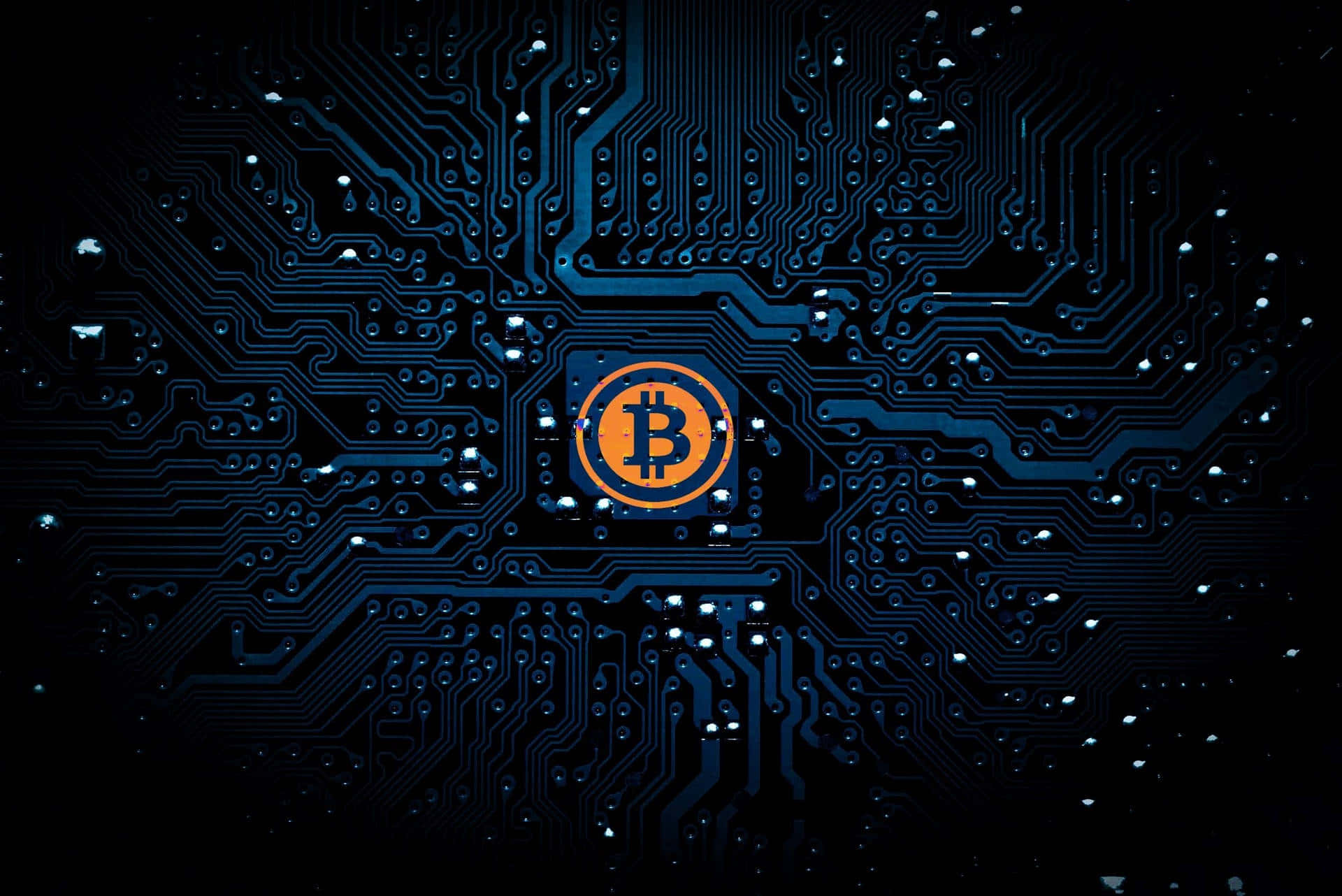 Motherboard 桌布 壁紙 — 一個發光的比特幣標誌，置中於一塊細節豐富的藍色電路板上，背景為黑色。