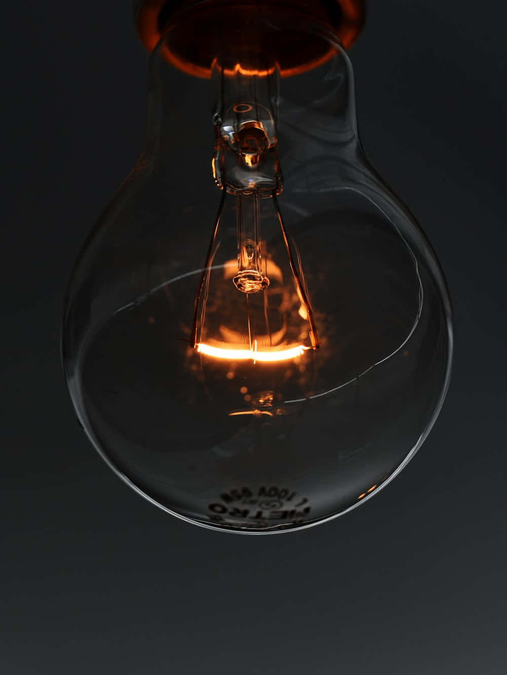 Electricity 桌布 壁紙 — 一個發光的白熾燈泡，帶有可見的燈絲和玻璃外殼，背景為深色。