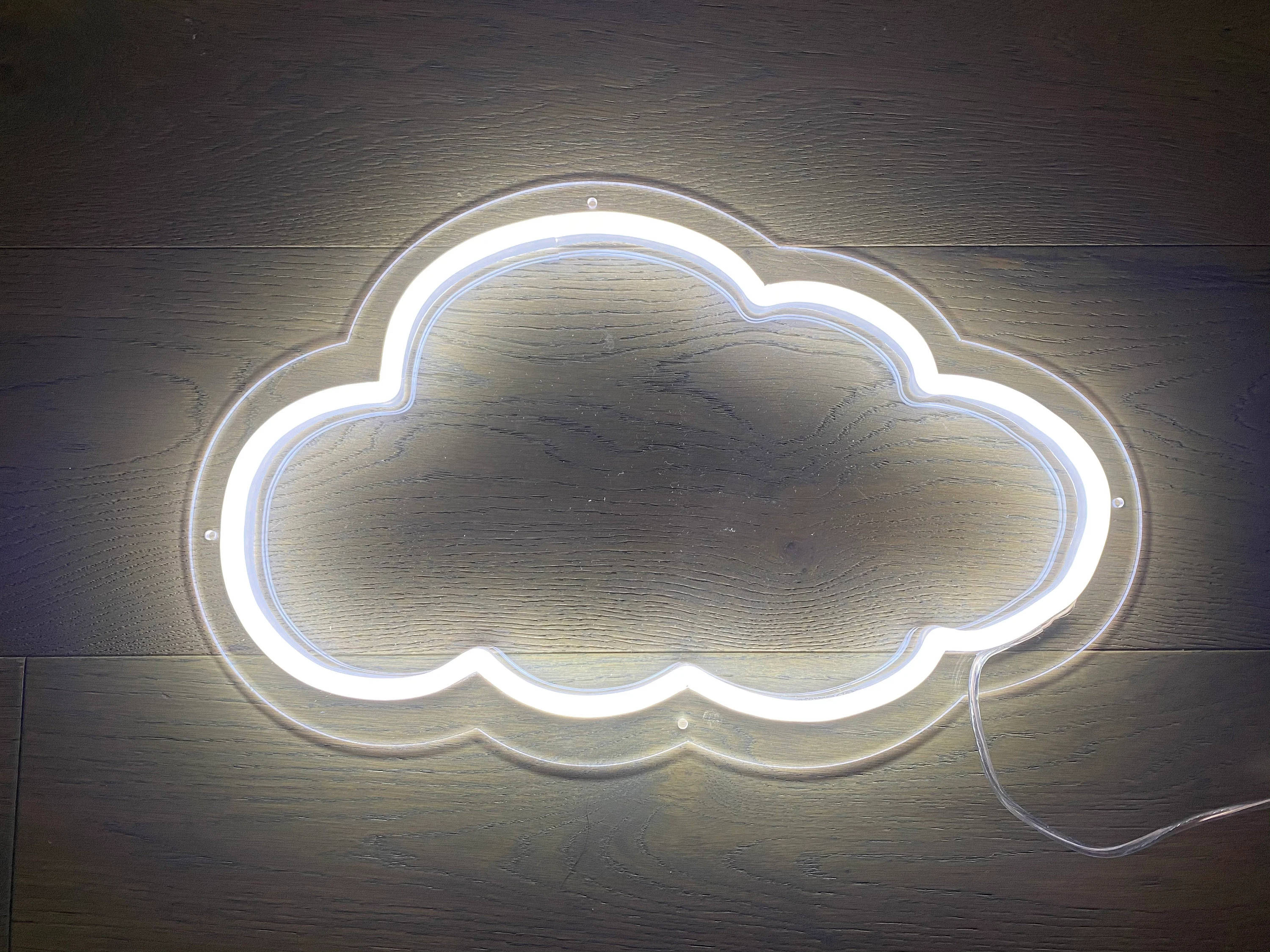 Cloud 桌布 壁紙 — 一個發光的白色霓虹雲燈具放在深色木地板上，投射出柔和的光線。