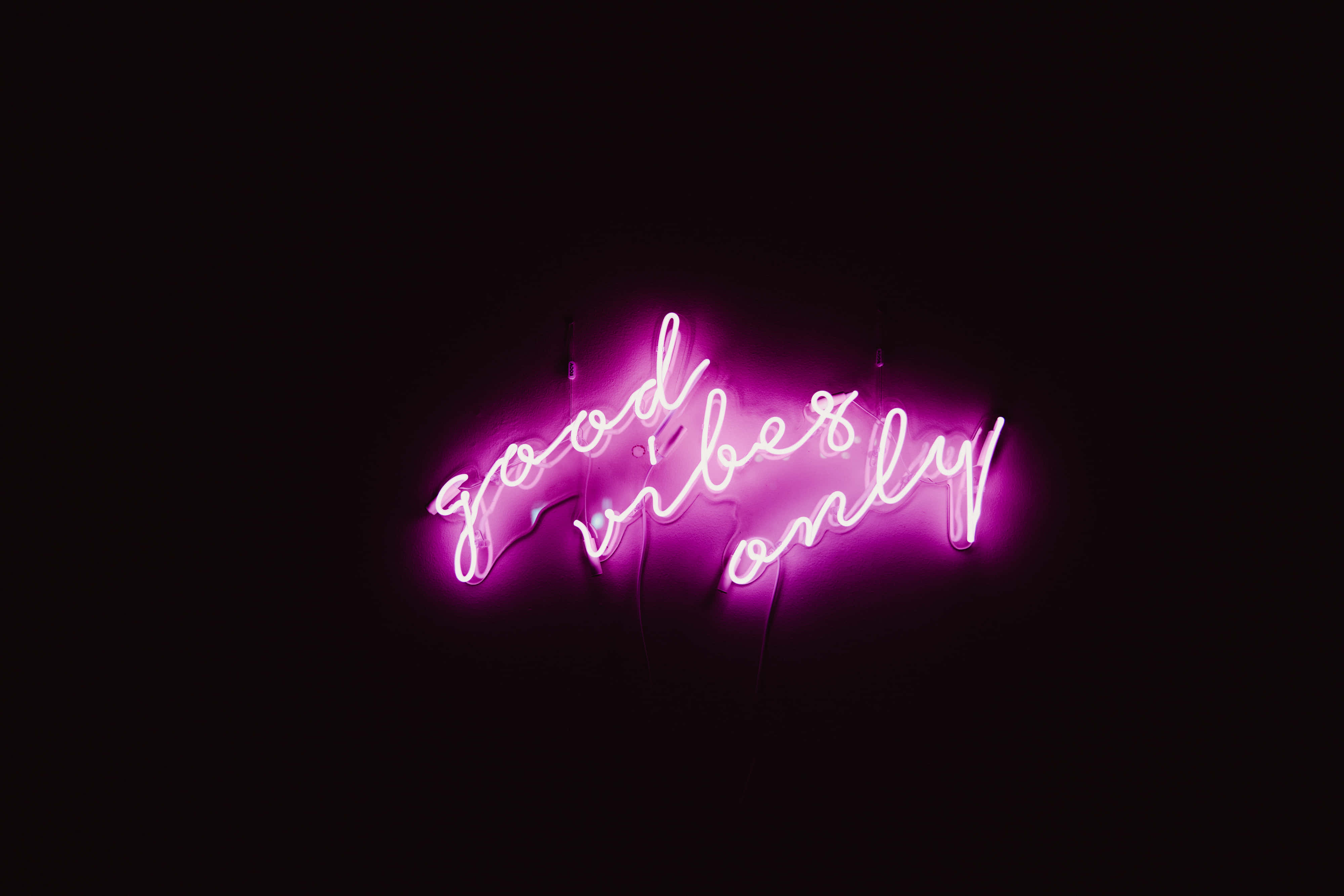 Beautiful Neon 桌布 壁紙 — 一個發光的粉紅色霓虹燈牌，上面寫著 good vibes only，在漆黑的背景下明亮地閃耀。