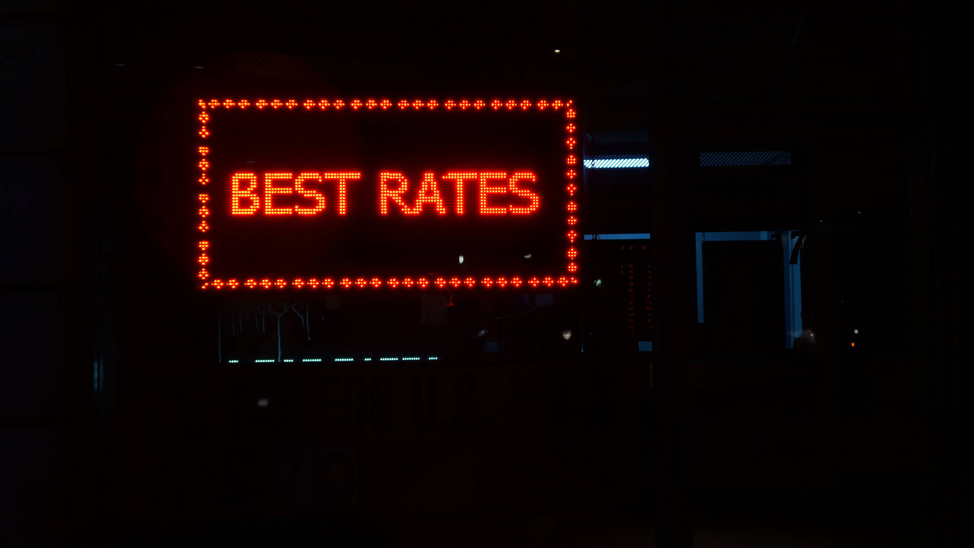 錢 桌布 壁紙 — 一個發光的紅色LED招牌，上面寫著「BEST RATES」，照亮了黑暗的城市夜景，背景中有微弱的藍色燈光。