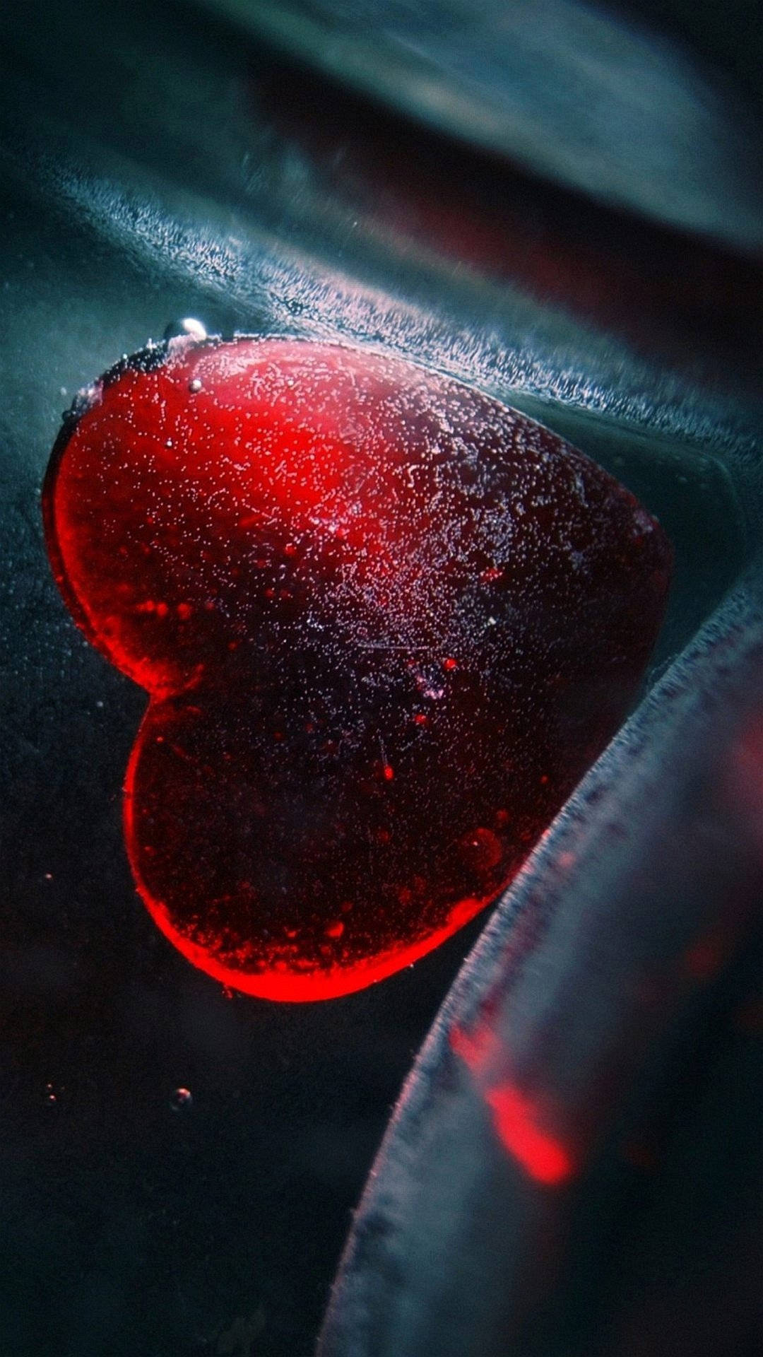 水晶動畫 桌布 壁紙 — 一個發光的紅色心形物體，嵌入在深色紋理玻璃中，帶有霜狀邊緣和散落的光粒子。