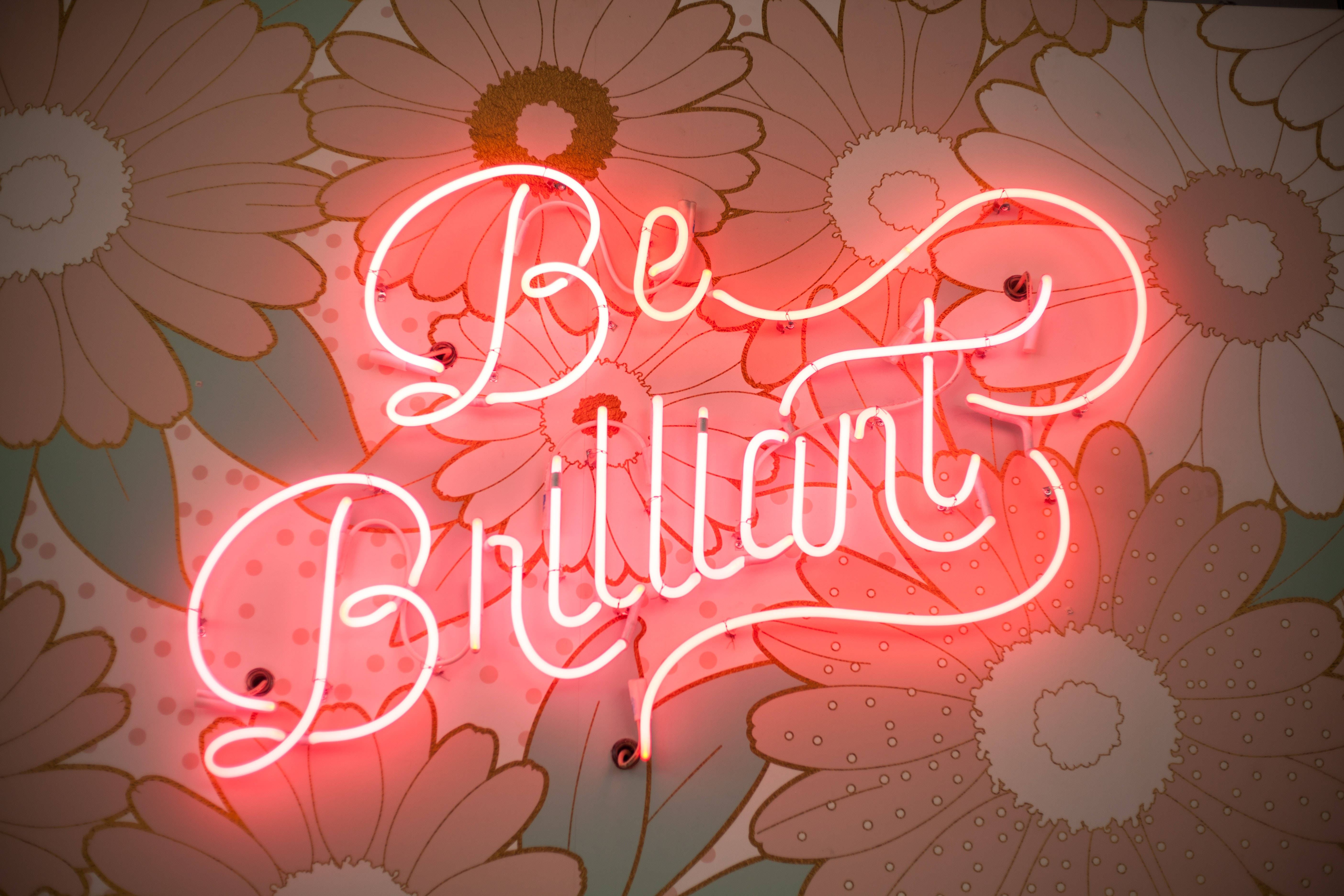 Best Quality 桌布 壁紙 — 一個發光的紅色霓虹燈牌，上面寫著「Be Brilliant」，在復古花卉壁紙背景下閃耀。