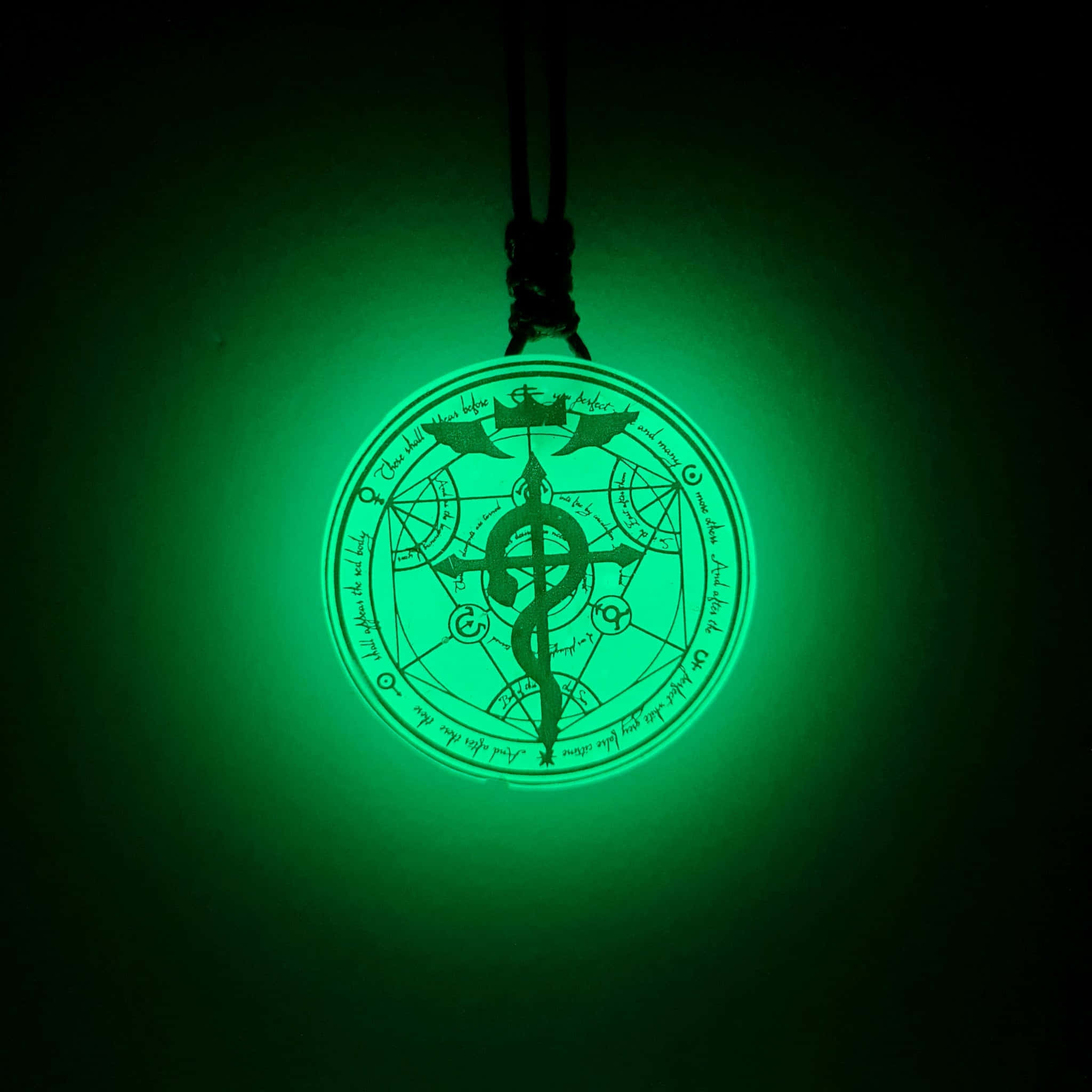 Alchemy 桌布 壁紙 — 一個發光的綠色圓形吊墜，帶有複雜的神秘符號和中央的雙蛇杖設計，懸掛在深色背景上。