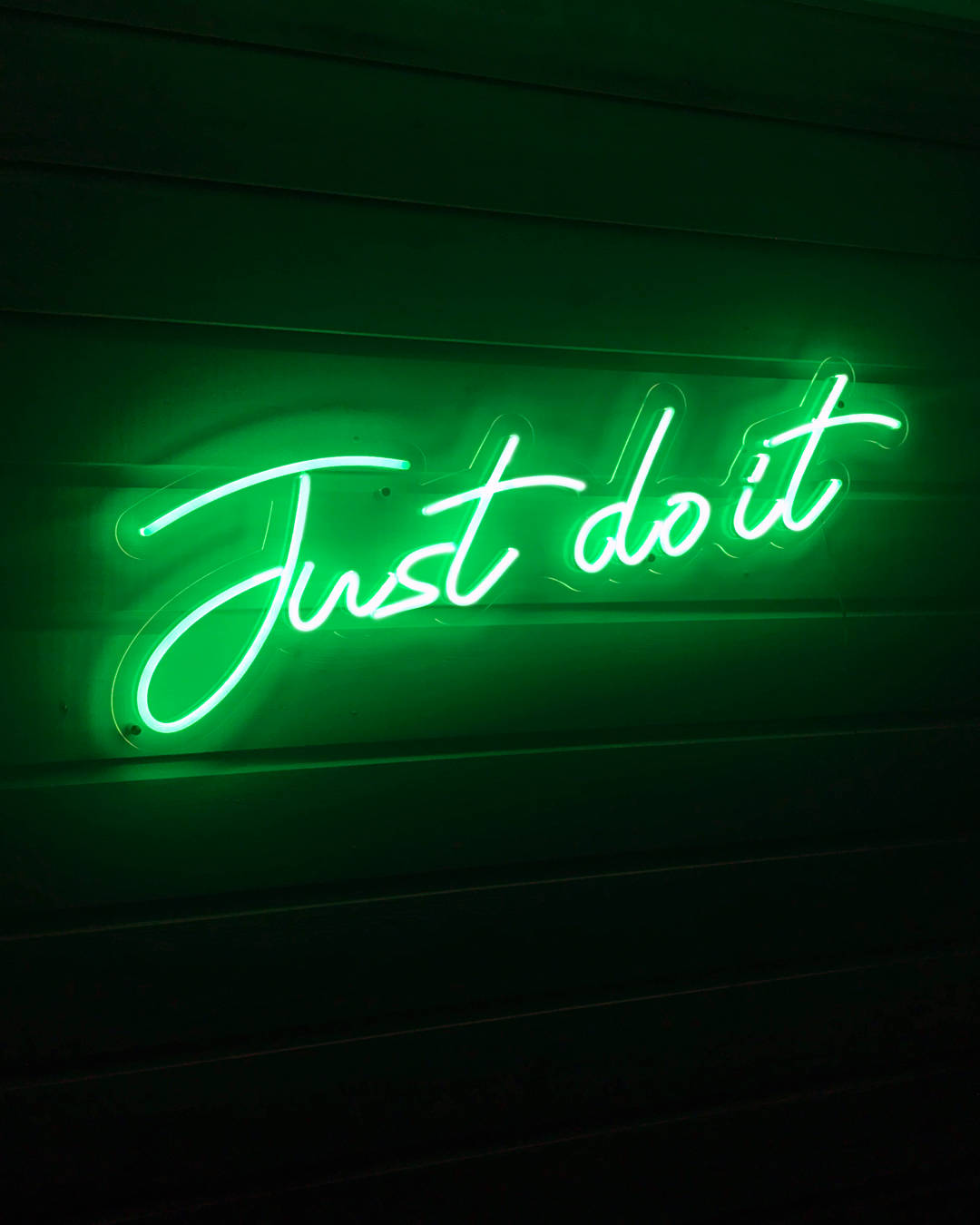 綠色美學 桌布 壁紙 — 一個發光的綠色霓虹燈牌，以草書寫着 'Just do it'，照亮了深色木牆。