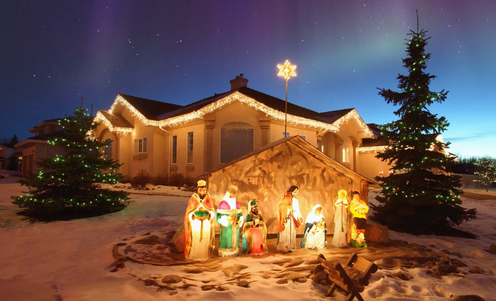 Nativity Scene 桌布 壁紙 — 一個發光的耶穌誕生場景，帶有發光的人物，站在雪前院，星空下，裝飾樹木。