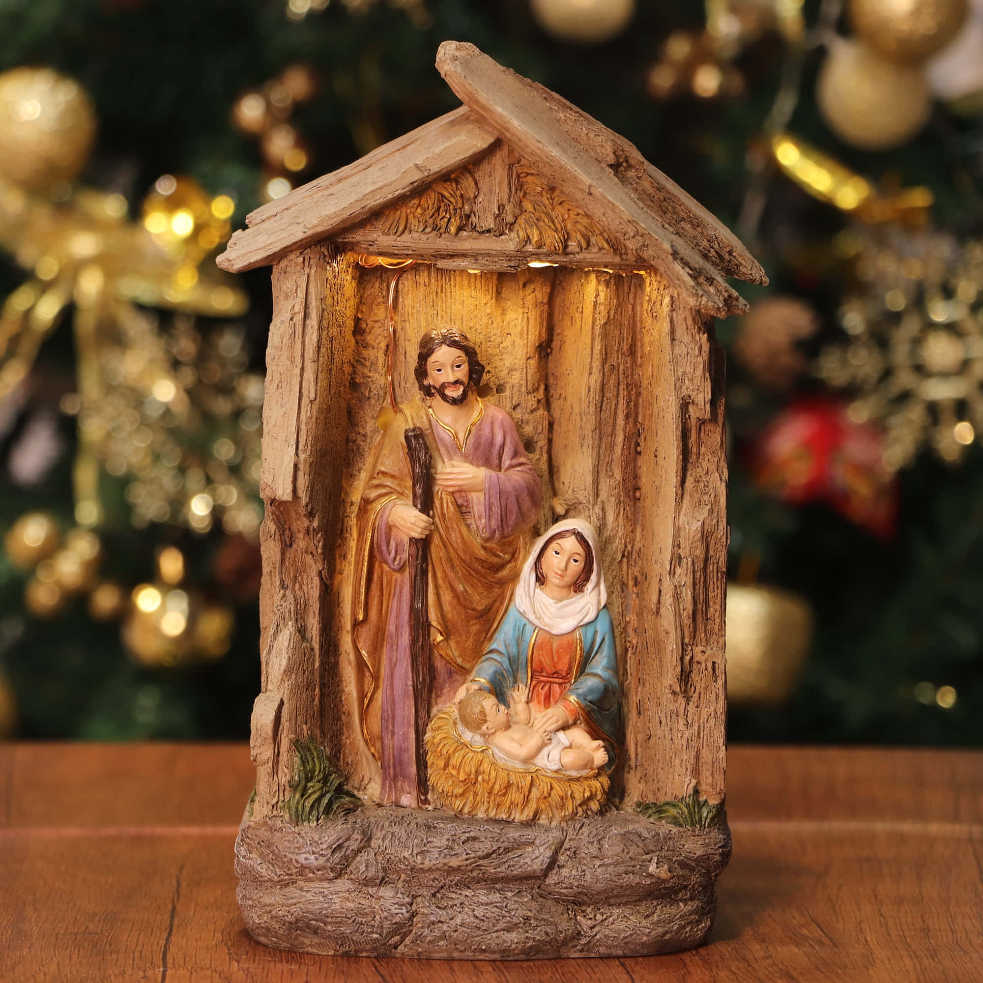 Nativity Scene 桌布 壁紙 — 一個發光的耶穌誕生場景公仔，約瑟、馬利亞和嬰兒耶穌在質樸的木製馬槽中，背景是模糊的聖誕樹。