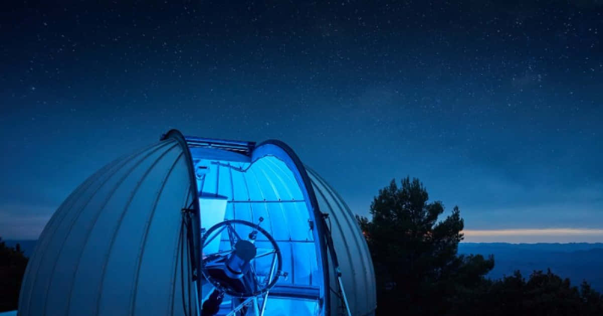 Observatory 桌布 壁紙 — 一個發光的藍色天文台圓頂在星空下敞開，遠方的山丘和樹木在下方形成剪影。