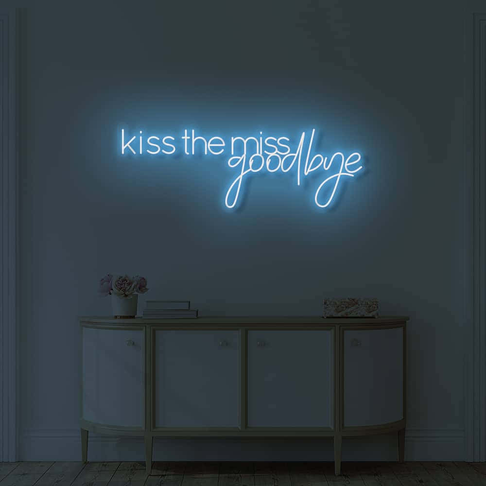 再見 桌布 壁紙 — 一個發光的藍色霓虹燈牌，上面寫著 kiss the miss goodbye，照亮了一個昏暗的房間，房間裡有一個木製玄關桌，上面擺放著鮮花和書籍。