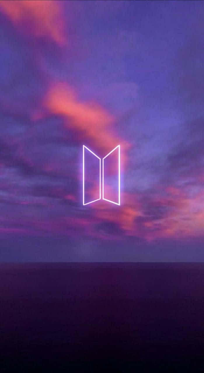Bts Icon 桌布 壁紙 — 一個發光的霓虹BTS標誌漂浮在充滿活力的紫色和粉紅色暮色天空上，下方是黑暗的海洋地平線。