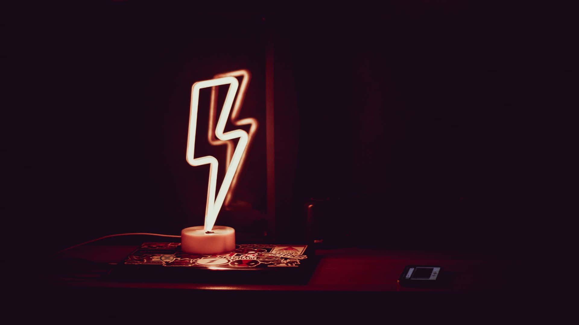 Glow In The Dark 桌布 壁紙 — 一個發光的霓虹閃電燈在黑暗的桌子上投射出溫暖的紅光，桌子上散落著硬幣和一部手機。