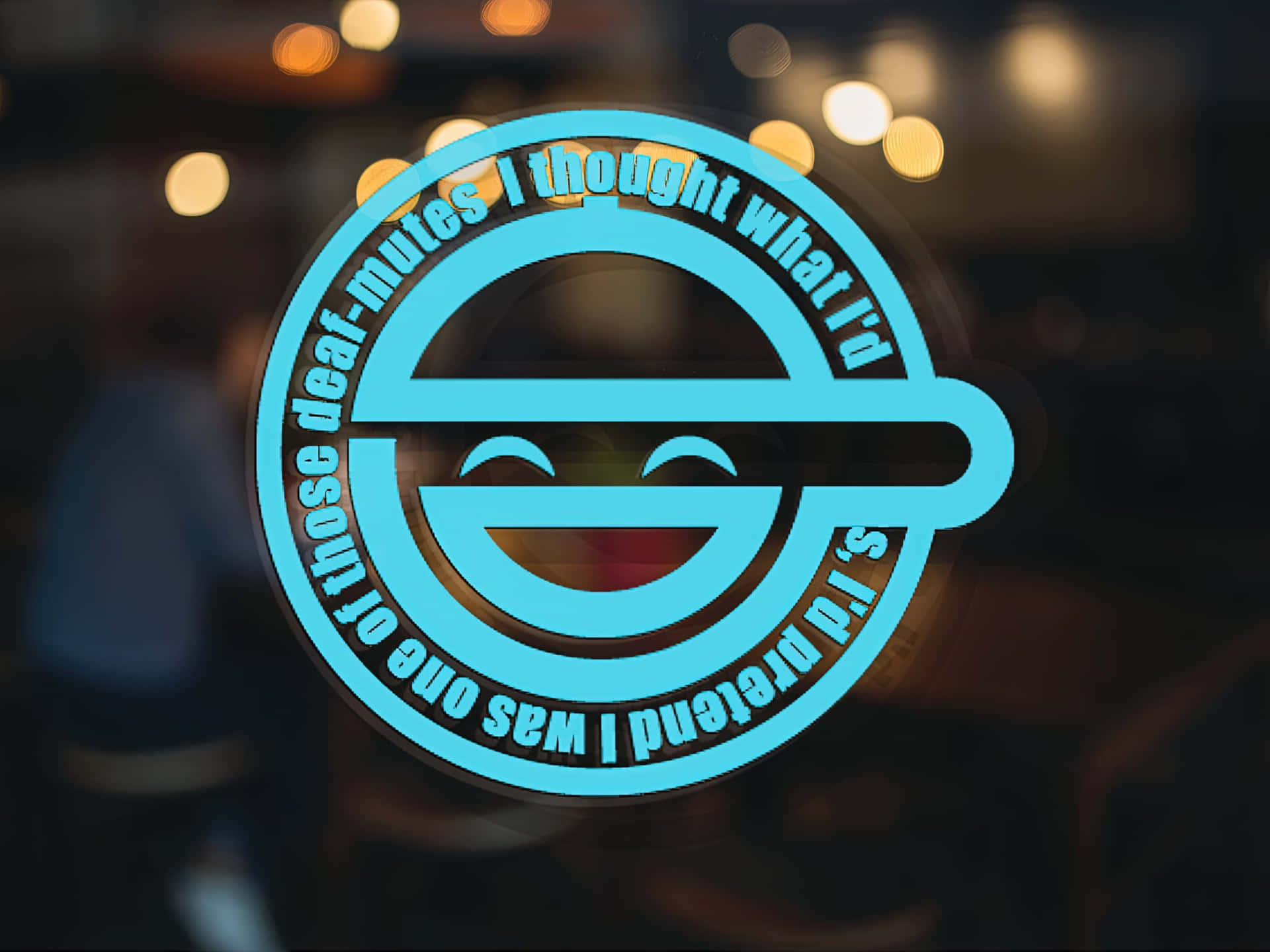 The Laughing Man 桌布 壁紙 — 一個發光的青色圓形貼紙，上面有笑臉和文字 'I was one of those deaf-mutes I thought what I'd s I'd pretend'，背景是模糊的暖色散景。
