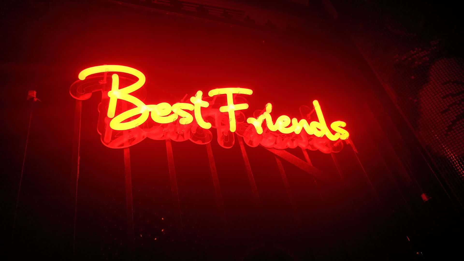 Best Friend 桌布 壁紙 — 一個發光的黃色霓虹燈牌，上面寫著 'Best Friends'，在黑暗背景下投射出溫暖的紅色光芒。