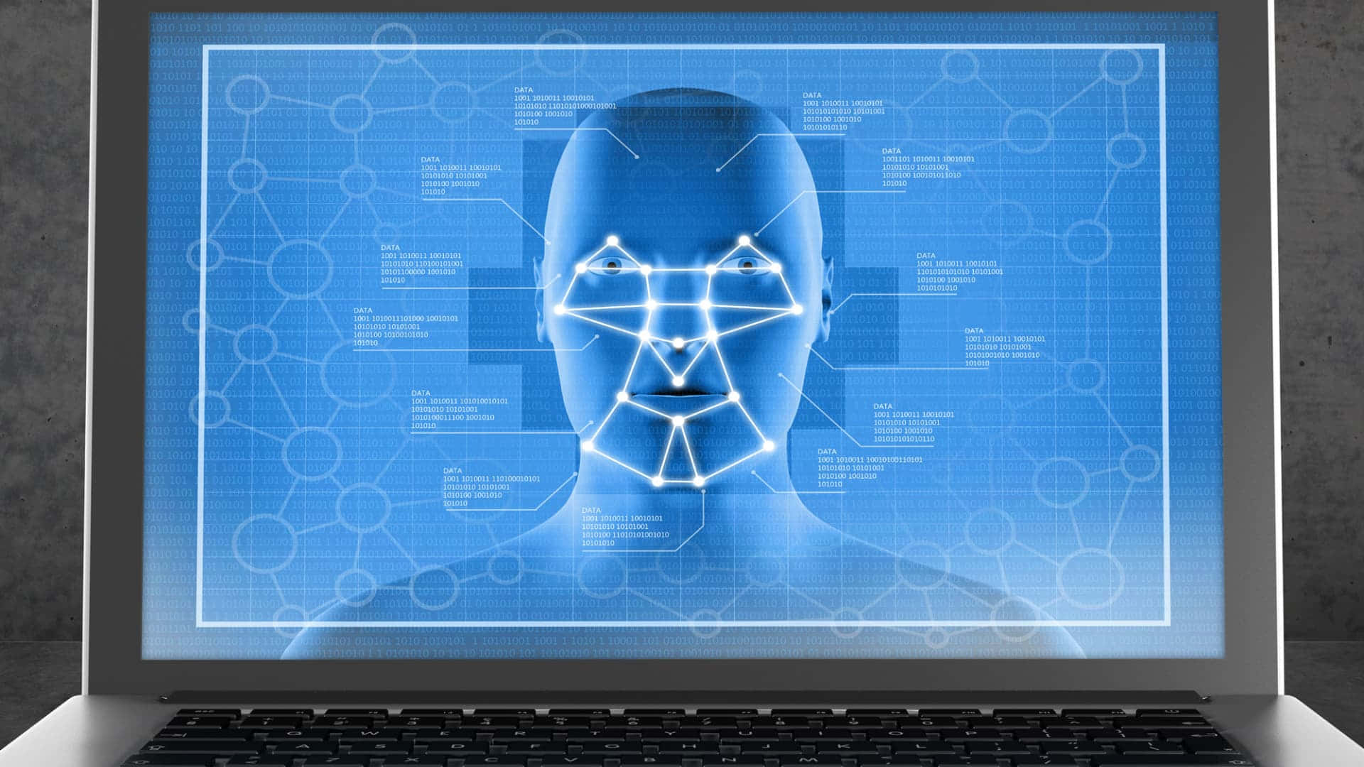 Face Recognition 桌布 壁紙 — 一個發光藍色全息人頭，帶有面部識別網格，顯示在筆記型電腦屏幕上，背景為混凝土牆。