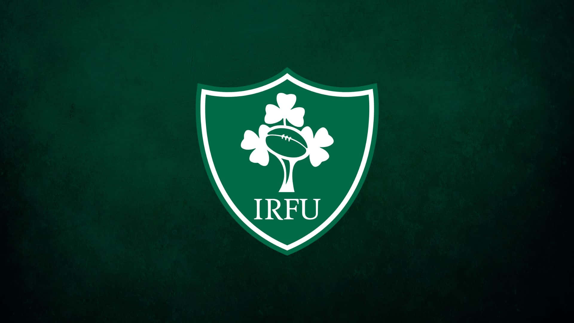 Ireland Rugby 桌布 壁紙 — 一個白色IRFU盾牌標誌，中央有酢漿草和欖球，置於有紋理的深綠色背景上。