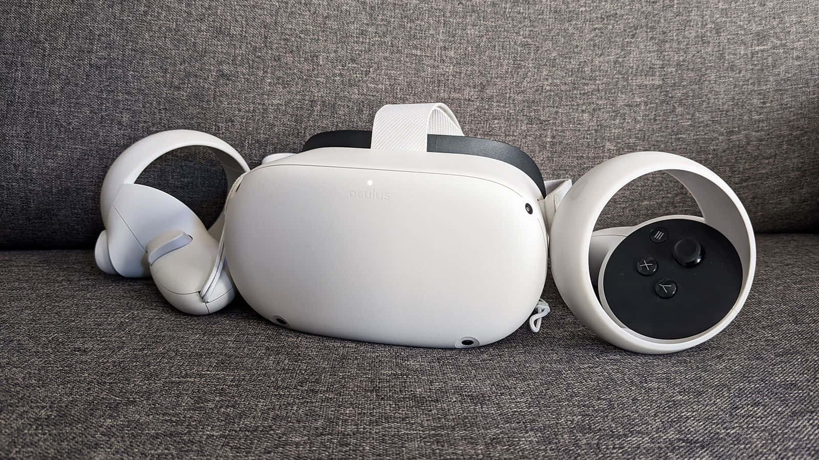Oculus Quest 2 桌布 壁紙 — 一個白色Oculus VR頭戴式裝置和控制器整齊地放在一張有紋理的灰色布藝梳化上。