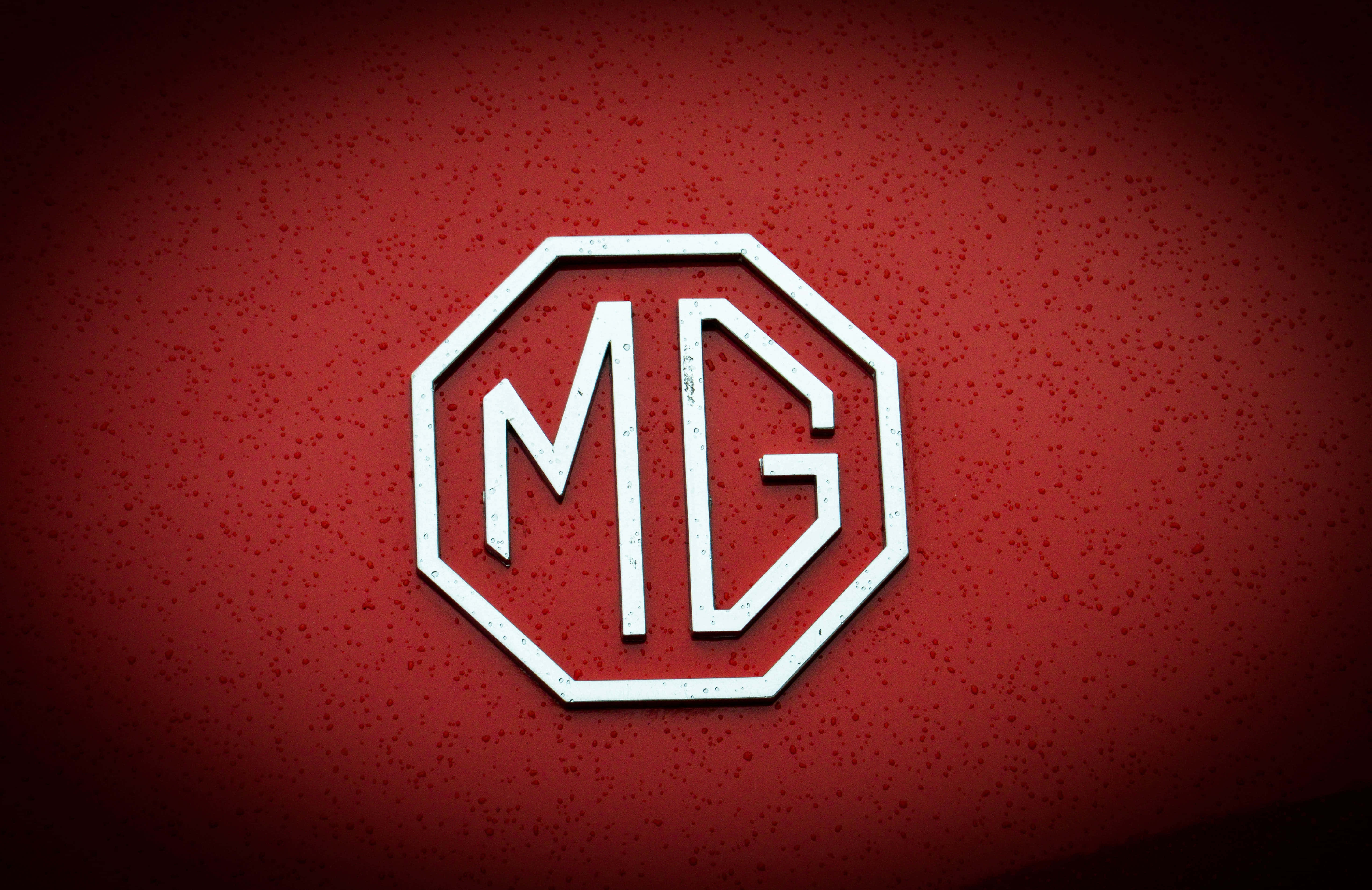 Mg 桌布 壁紙 — 一個白色八角形MG標誌，帶有磨損紋理，在帶有漸變照明的斑駁深紅色背景上脫穎而出。
