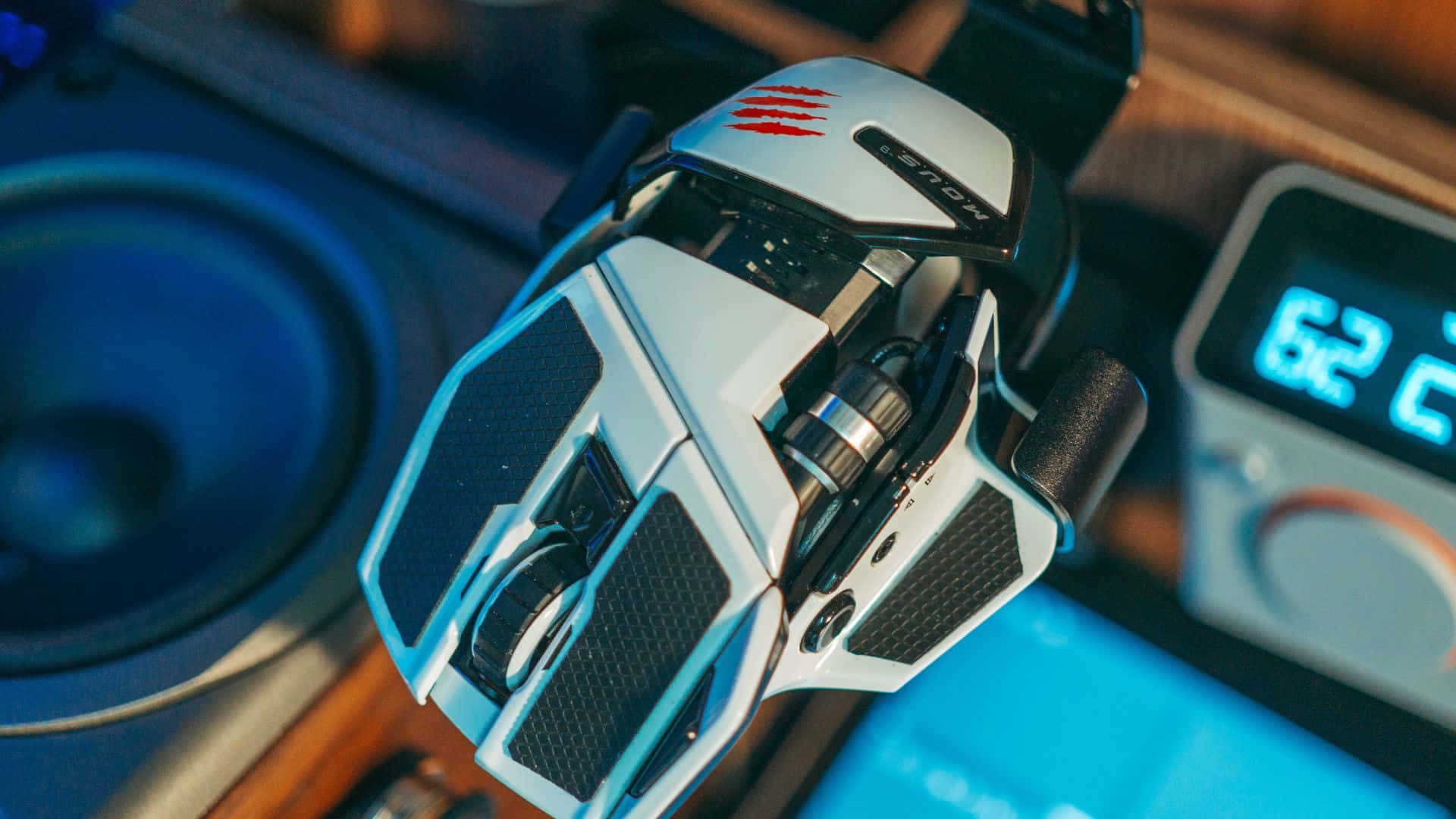 Gaming Mice 桌布 壁紙 — 一個白色和黑色遊戲滑鼠的特寫，帶有紅色爪痕，放在木桌上，旁邊有一個揚聲器和一個數位時鐘。