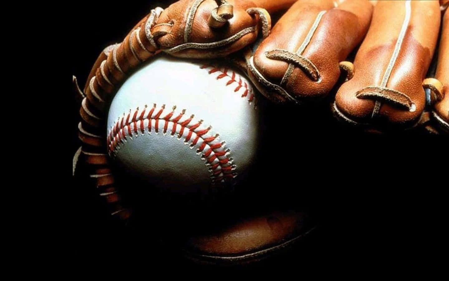 Cool Baseball 桌布 壁紙 — 一個白色帶紅色縫線的棒球，放在一個磨損的棕色皮手套中，背景為黑色，特寫鏡頭。