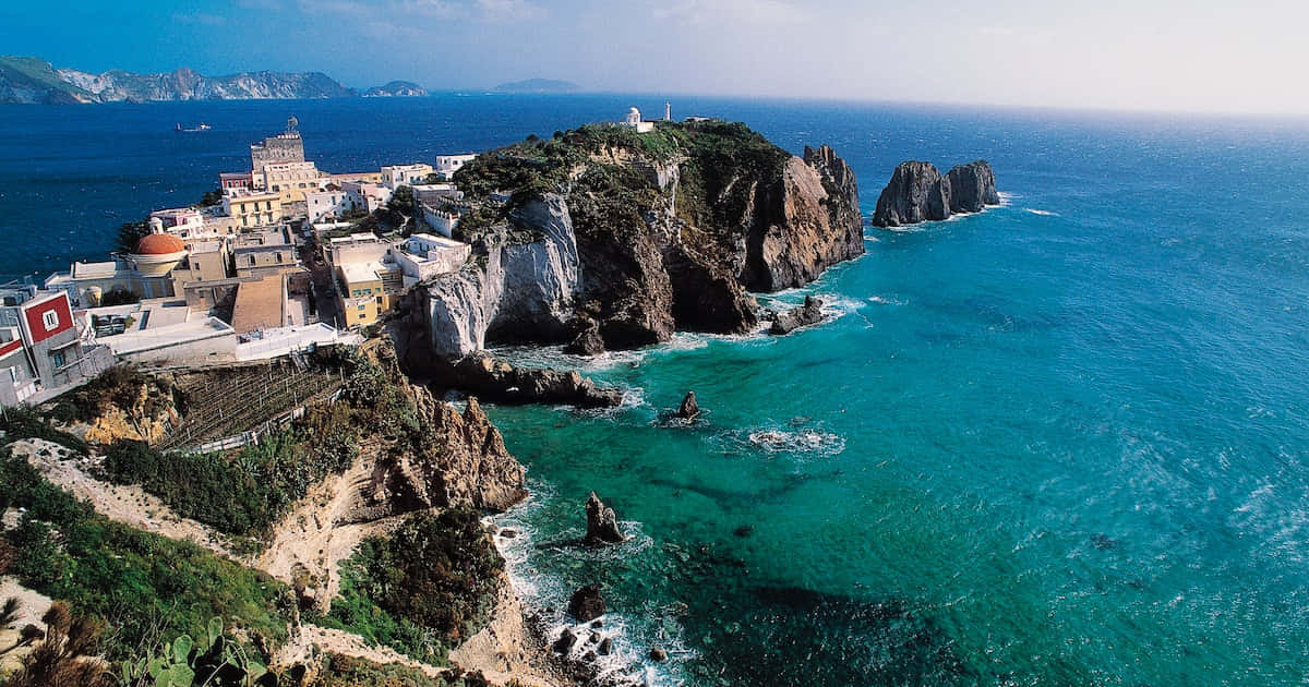 Italian Island 桌布 壁紙 — 一個白色建築的懸崖海邊村莊，依附在崎嶇的岩石上，俯瞰著清澈藍天下碧綠的海水。
