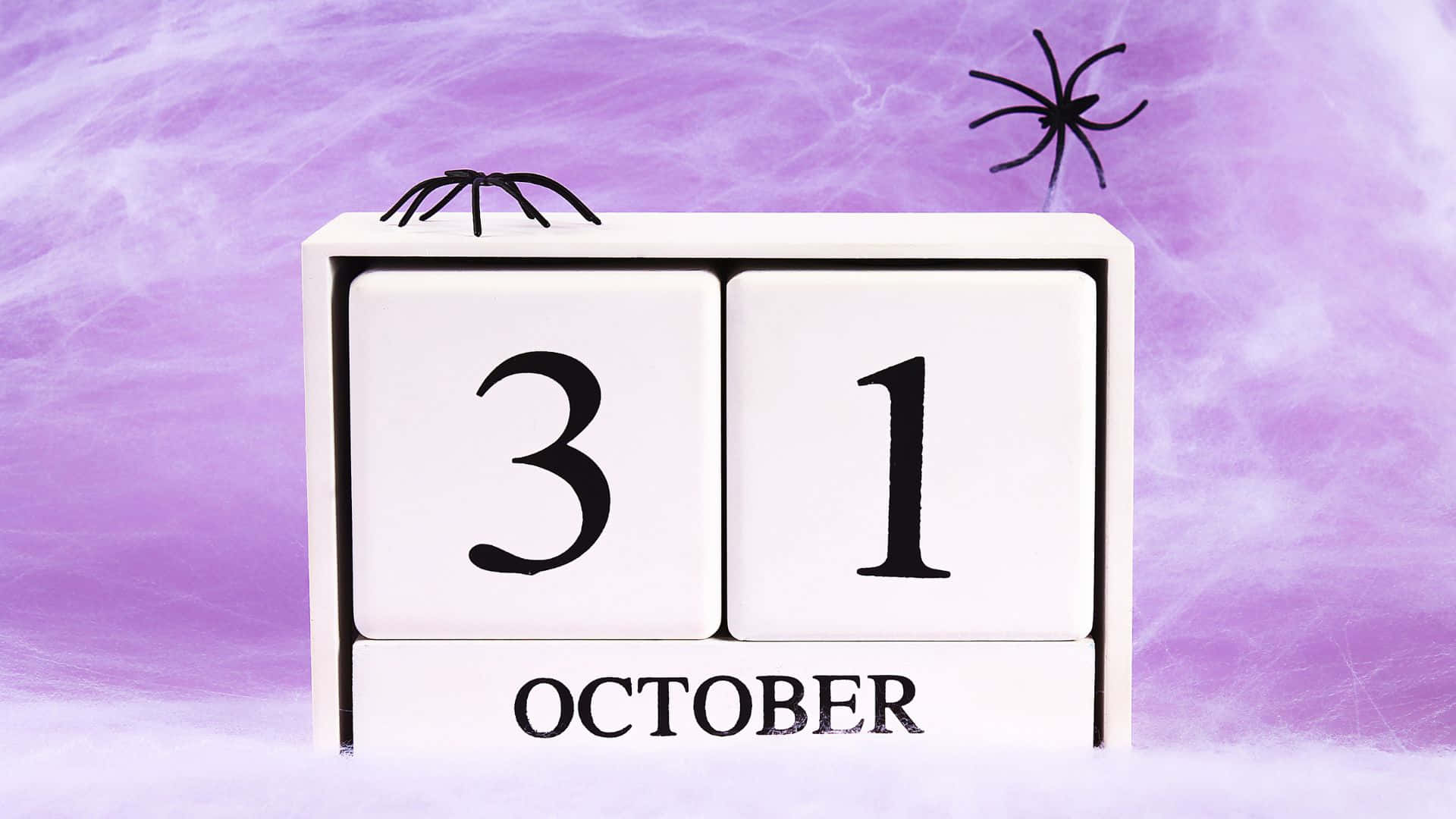 October 31st 桌布 壁紙 — 一個白色木製日曆塊在旋轉的紫色煙霧背景上顯示10月31日，並有兩隻黑色塑膠蜘蛛。