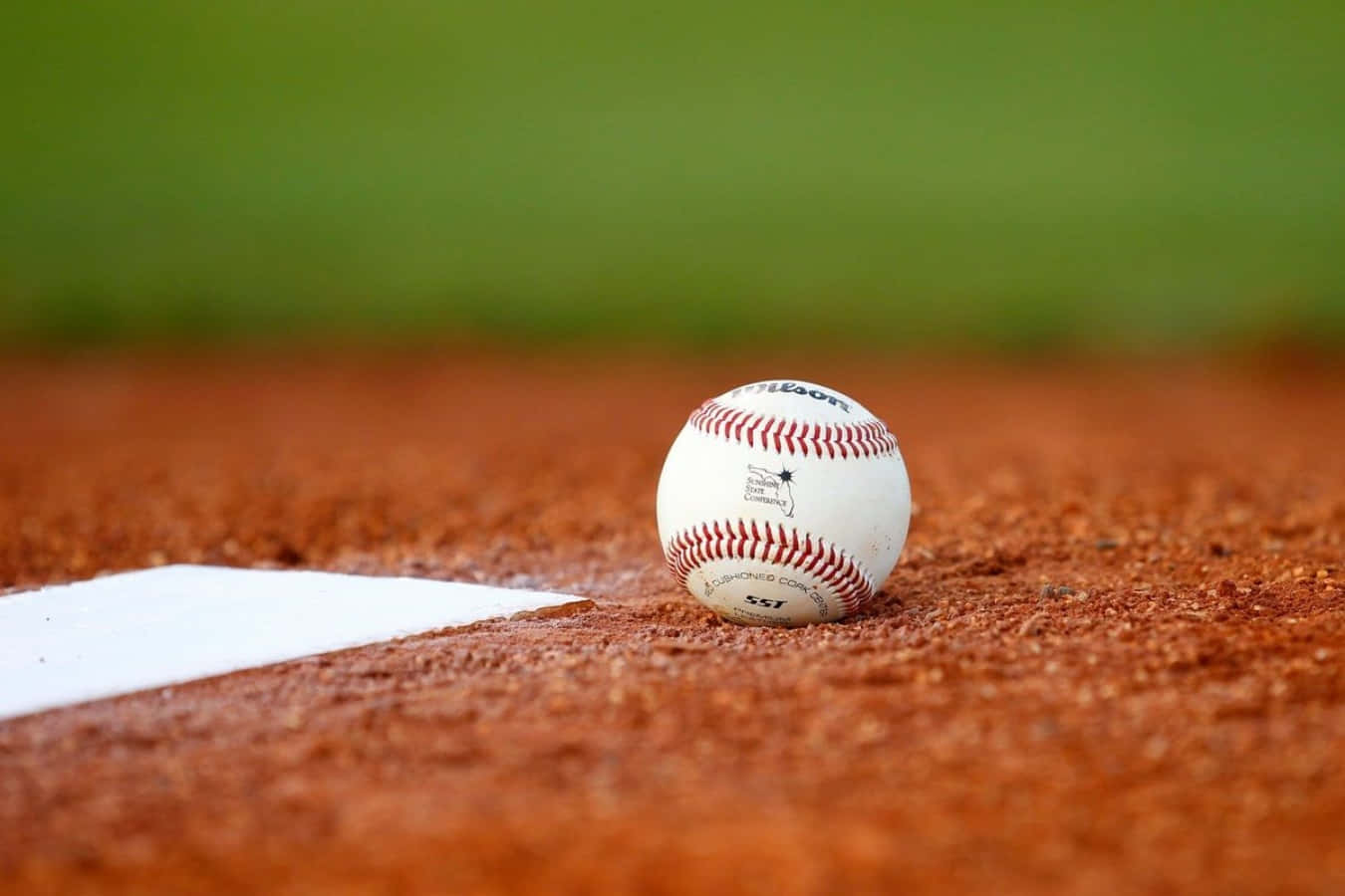 Cool Baseball 桌布 壁紙 — 一個白色棒球嘅特寫，有紅色縫線，放喺紅褐色泥土上面，旁邊係一個白色本壘板。