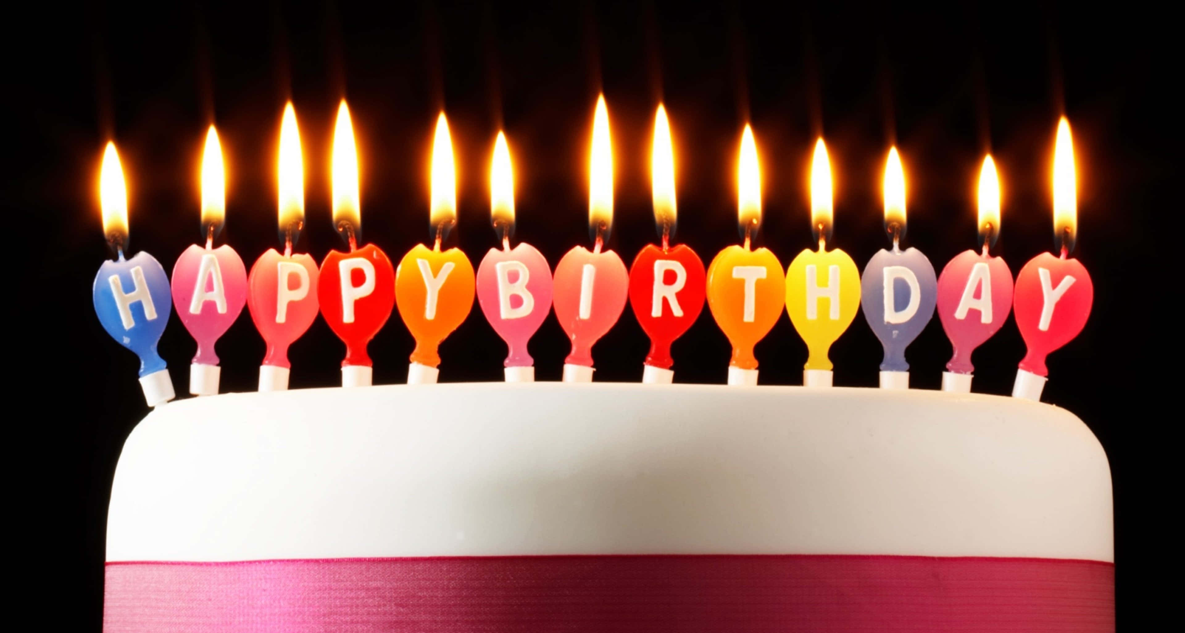 生日祝福 桌布 壁紙 — 一個白色生日蛋糕，上面有彩虹色心形蠟燭，在黑色背景上拼出「HAPPY BIRTHDAY」。