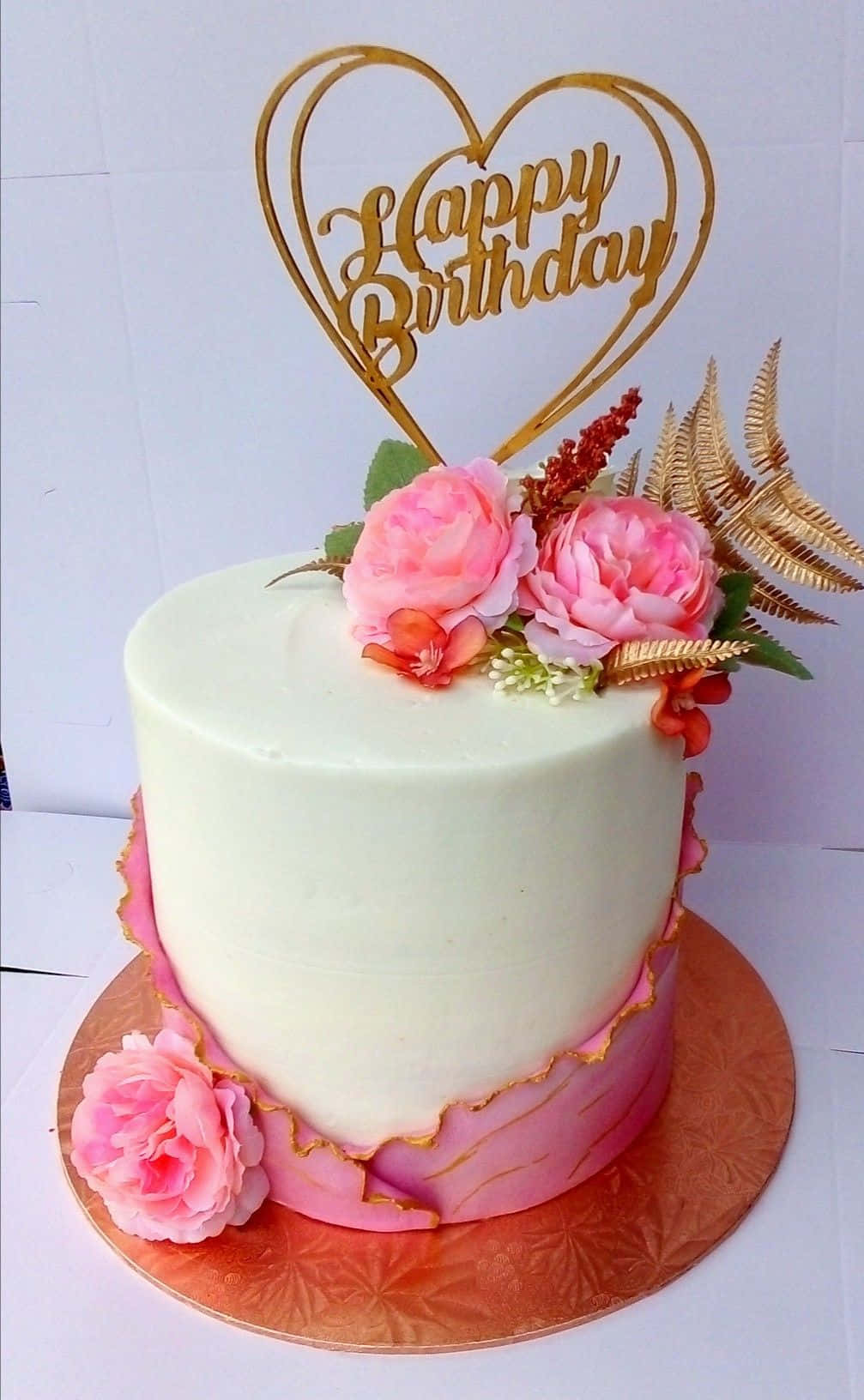 生日蛋糕 桌布 壁紙 — 一個白色生日蛋糕，飾有粉紅玫瑰、金色蕨類植物和一個心形裝飾，上面寫著「Happy Birthday」。