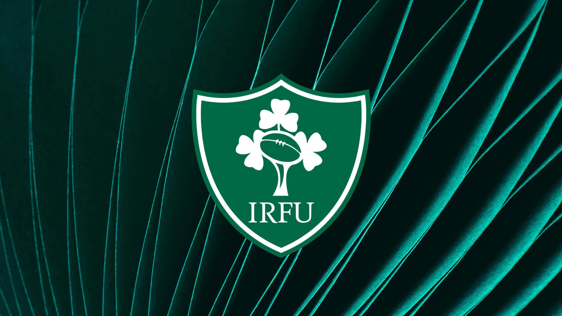 Ireland Rugby 桌布 壁紙 — 一個白色的愛爾蘭欖球聯盟徽章，上面有三個三葉草和一個欖球，位於有紋理的青綠色天鵝絨背景中央。