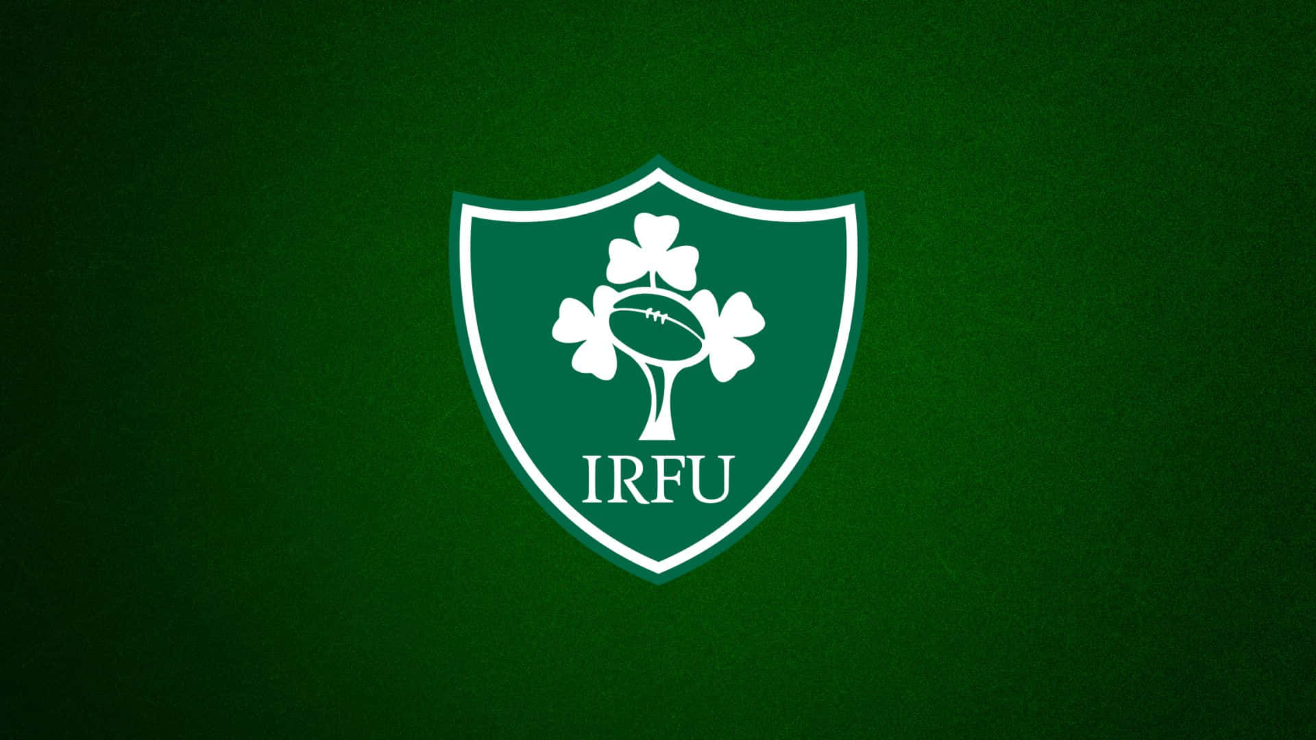 Ireland Rugby 桌布 壁紙 — 一個白色的愛爾蘭欖球聯盟徽章，中央有酢漿草和欖球，置於有紋理的深綠色背景上。