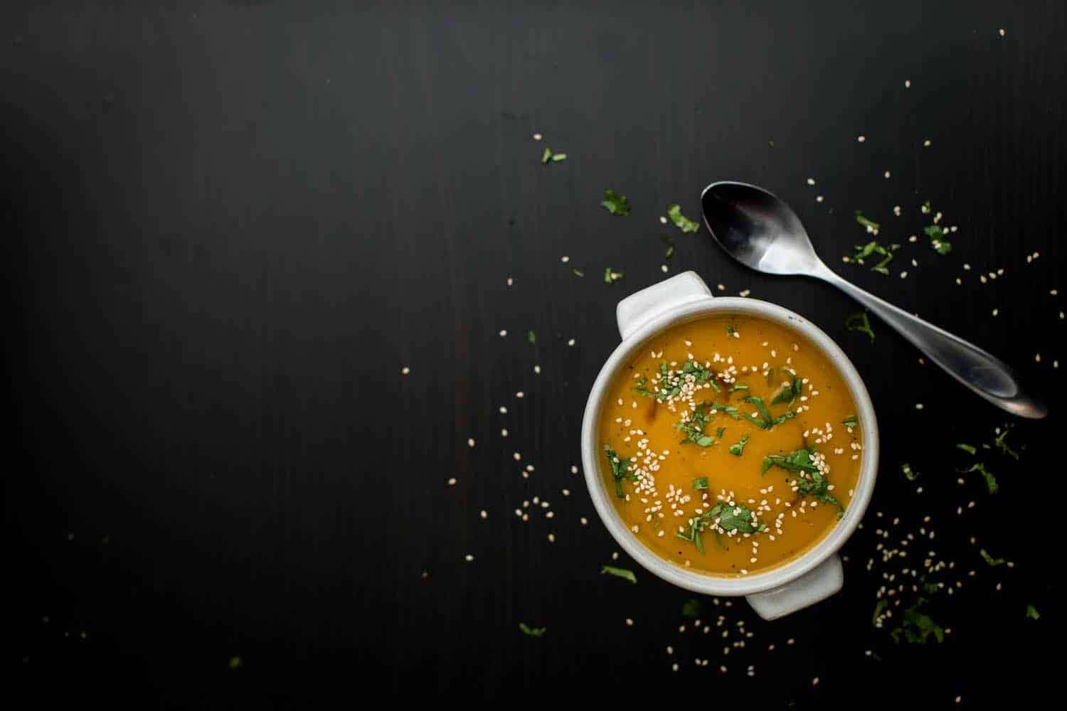 Soup 桌布 壁紙 — 一個白色碗中的奶油橙色湯，上面撒有芝麻和新鮮香草，放在深色質樸的木質表面上。