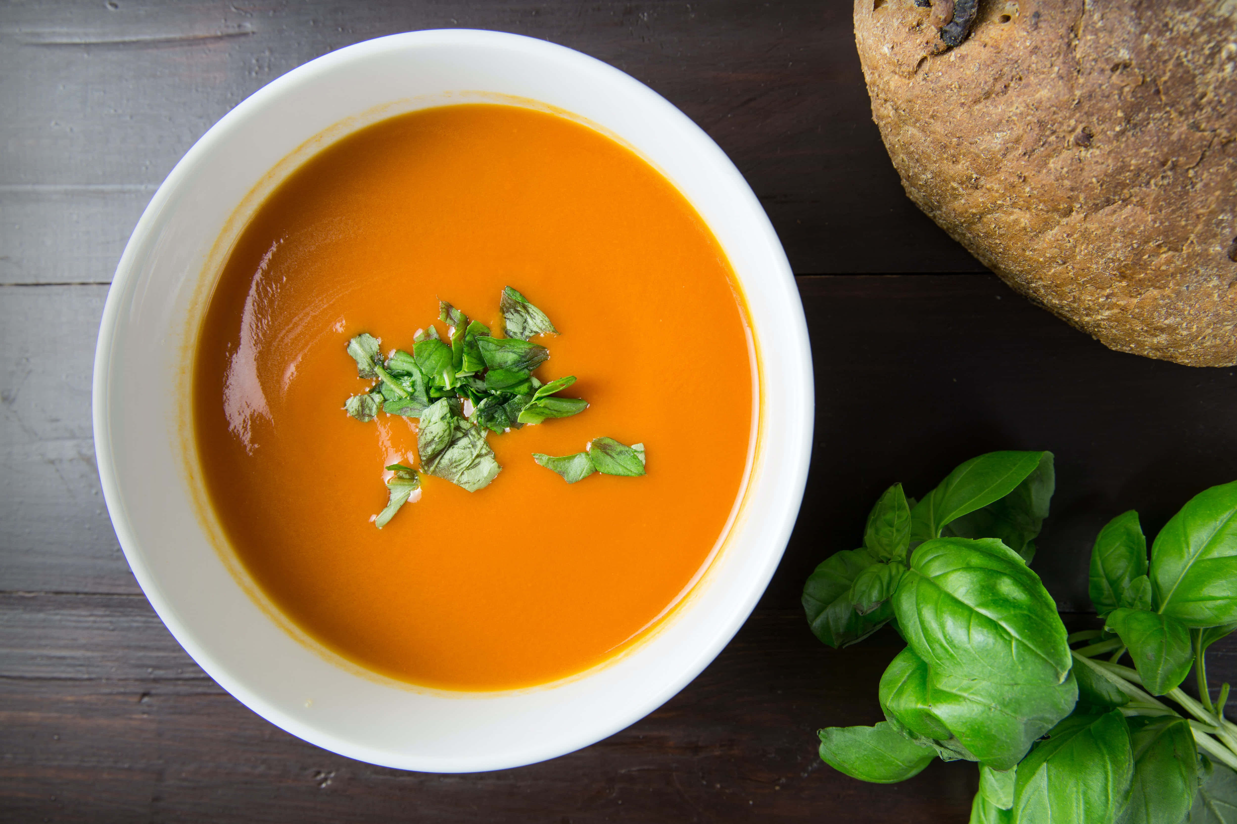 Soup 桌布 壁紙 — 一個白色碗中的奶油橙色湯，上面放著新鮮羅勒葉，旁邊有一條鄉村麵包放在深色木桌上。