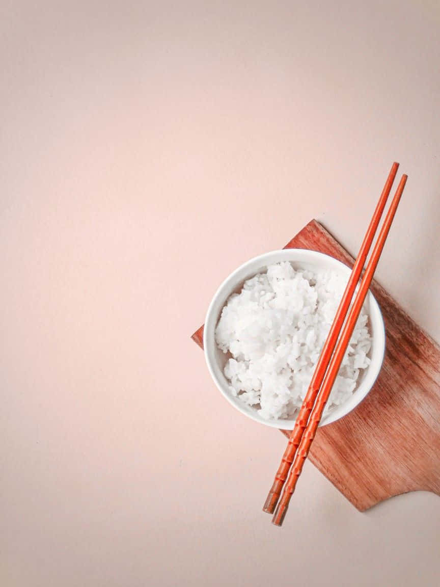 Minimalist Food 桌布 壁紙 — 一個白色碗盛載 fluffy 蒸飯，配橙色筷子，放在木板上，背景係柔和蜜桃色。