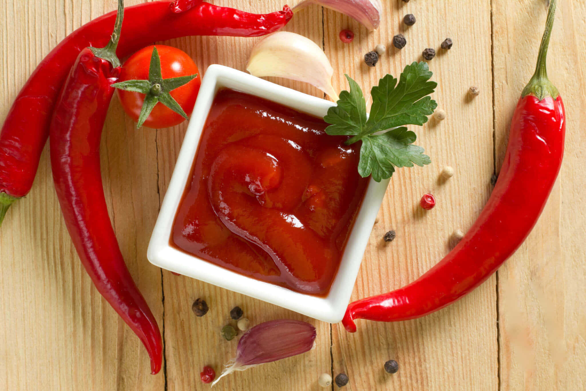 Red Sauce 桌布 壁紙 — 一個白色碗裝著光澤的紅色醬汁，周圍是新鮮辣椒、番茄、大蒜和香草，放在木質表面上。