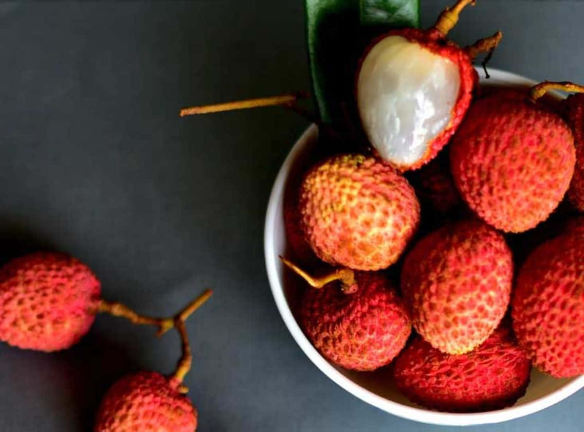 Red Fruit 桌布 壁紙 — 一個白色碗裡裝著鮮紅色的荔枝，其中一個剝了皮，露出半透明的白色果肉，背景是深灰色。