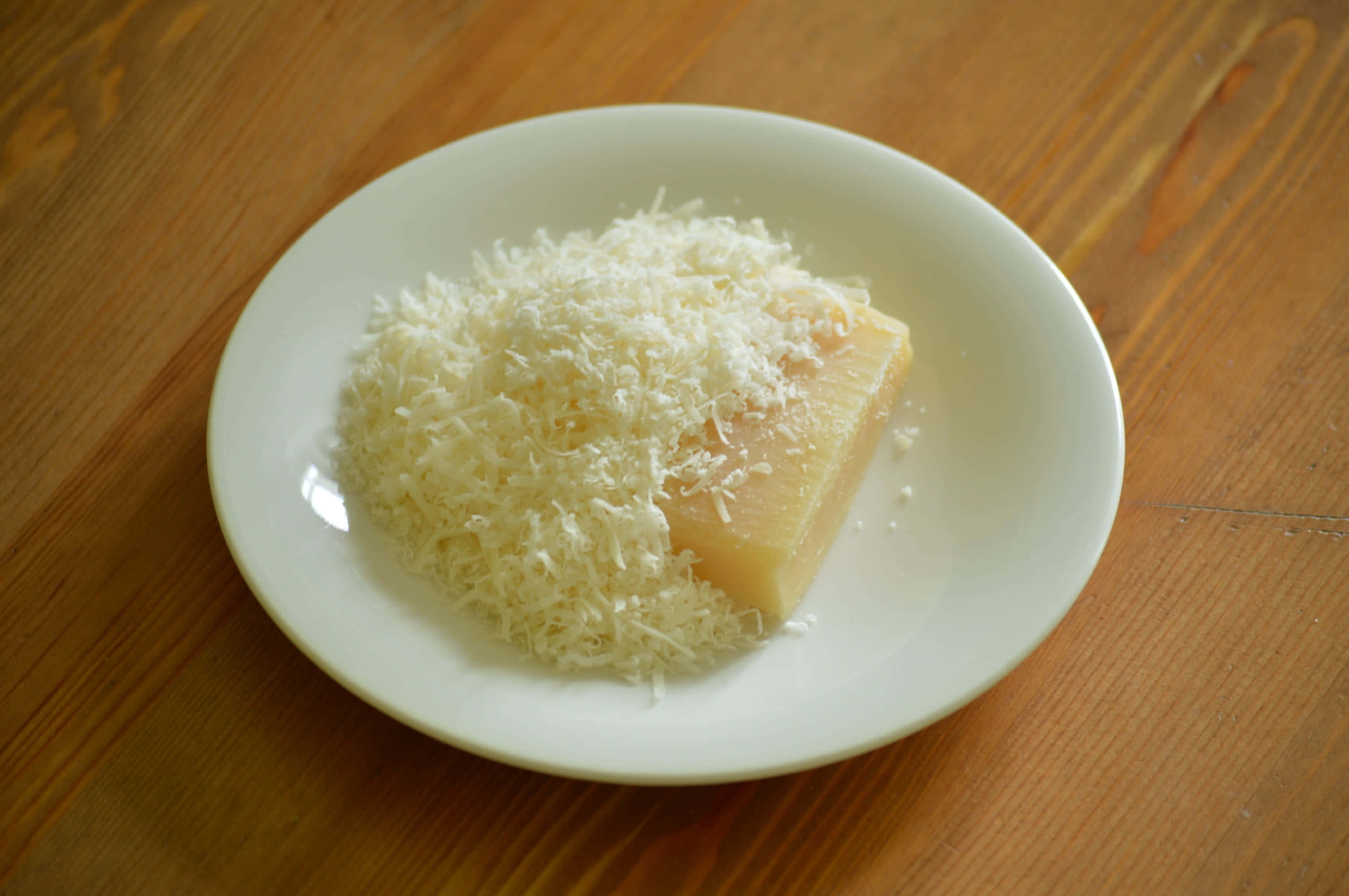 Cheese 桌布 壁紙 — 一個白色碟子盛著一塊硬芝士和一堆磨碎的芝士，放在溫暖的木桌上。