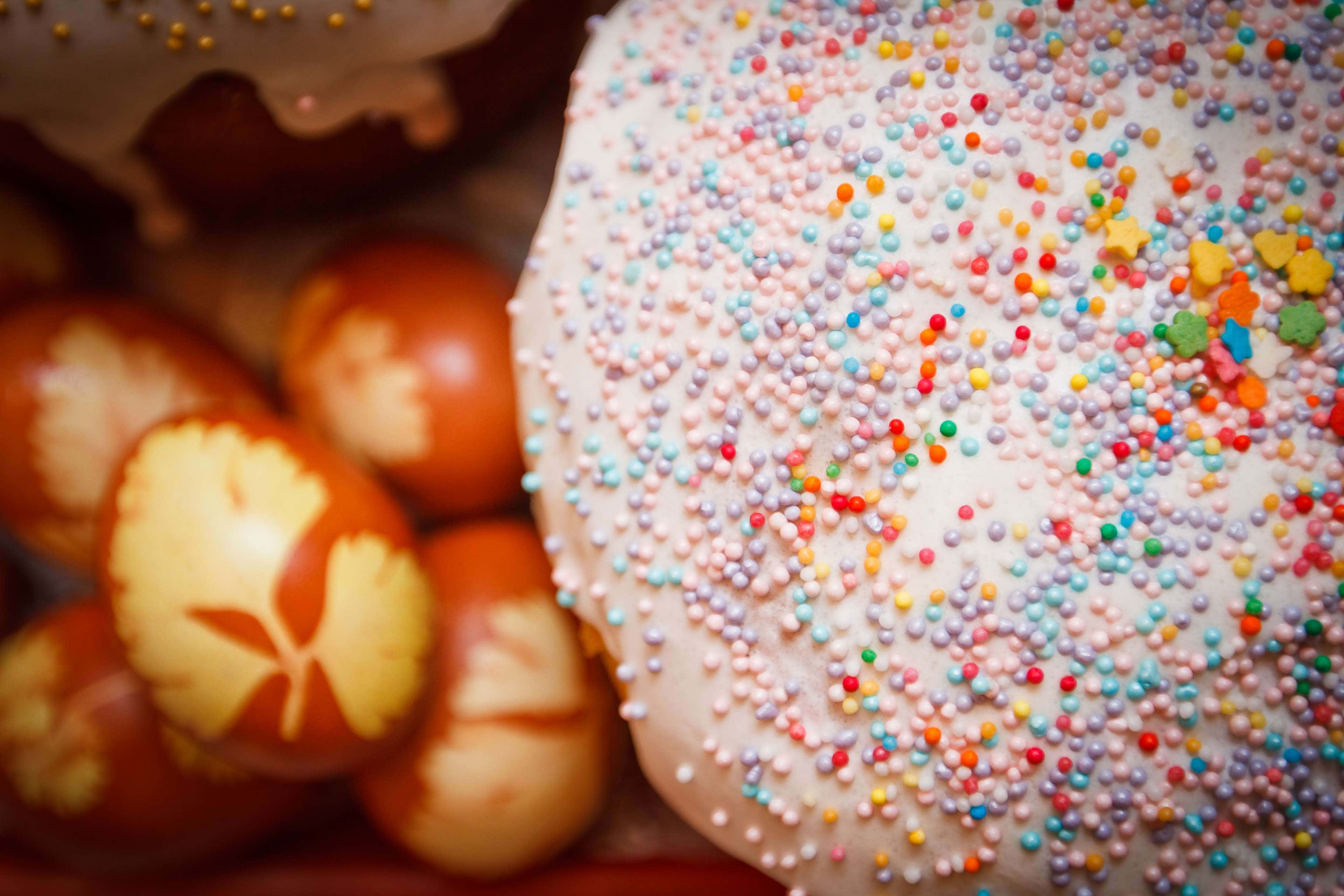 donuts 桌布 壁紙 — 一個白色糖霜蛋糕的特寫，上面覆蓋著彩色糖粒，旁邊是圖案精緻的棕色雞蛋。