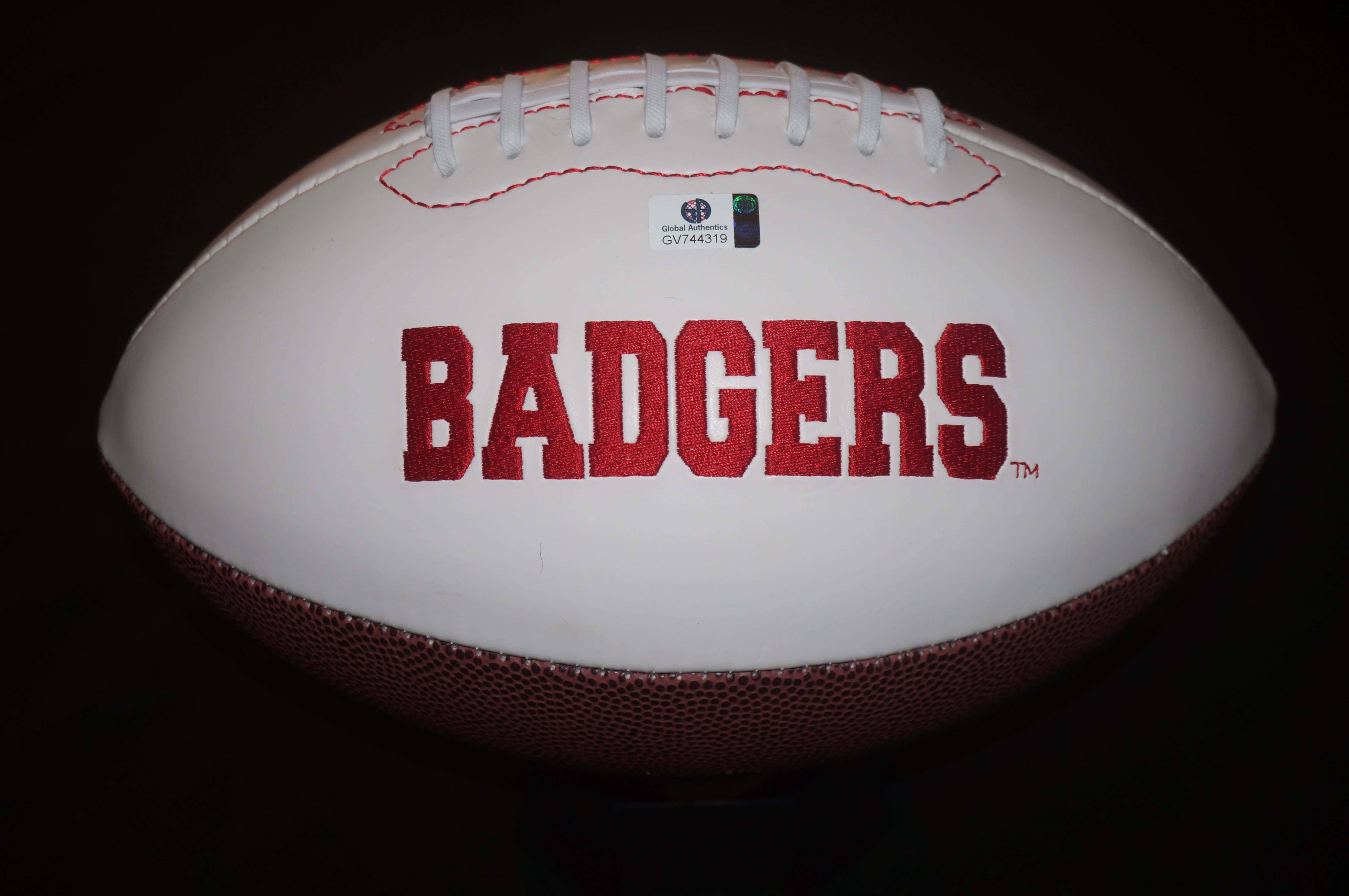 Wisconsin Badgers 桌布 壁紙 — 一個白色美式足球，上面有粗體紅色 'BADGERS' 字樣和白色鞋帶，靠在深色背景上。