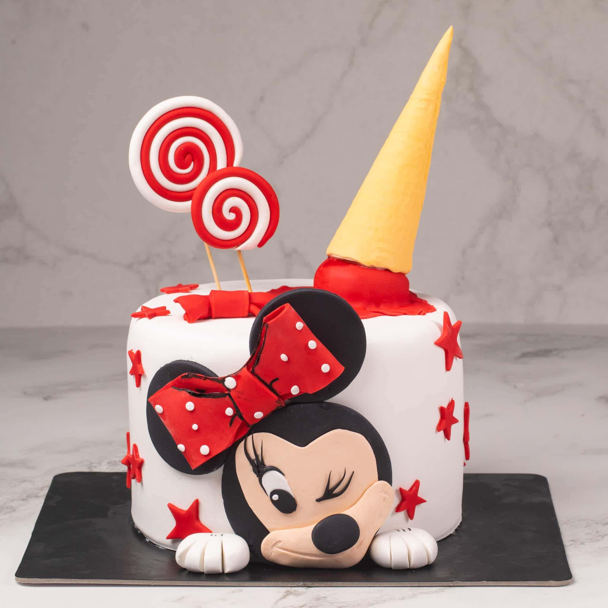 Cake Fondant 桌布 壁紙 — 一個白色翻糖蛋糕上有一個3D米妮老鼠的臉從邊緣探出，頂部有紅色星星和棒棒糖。